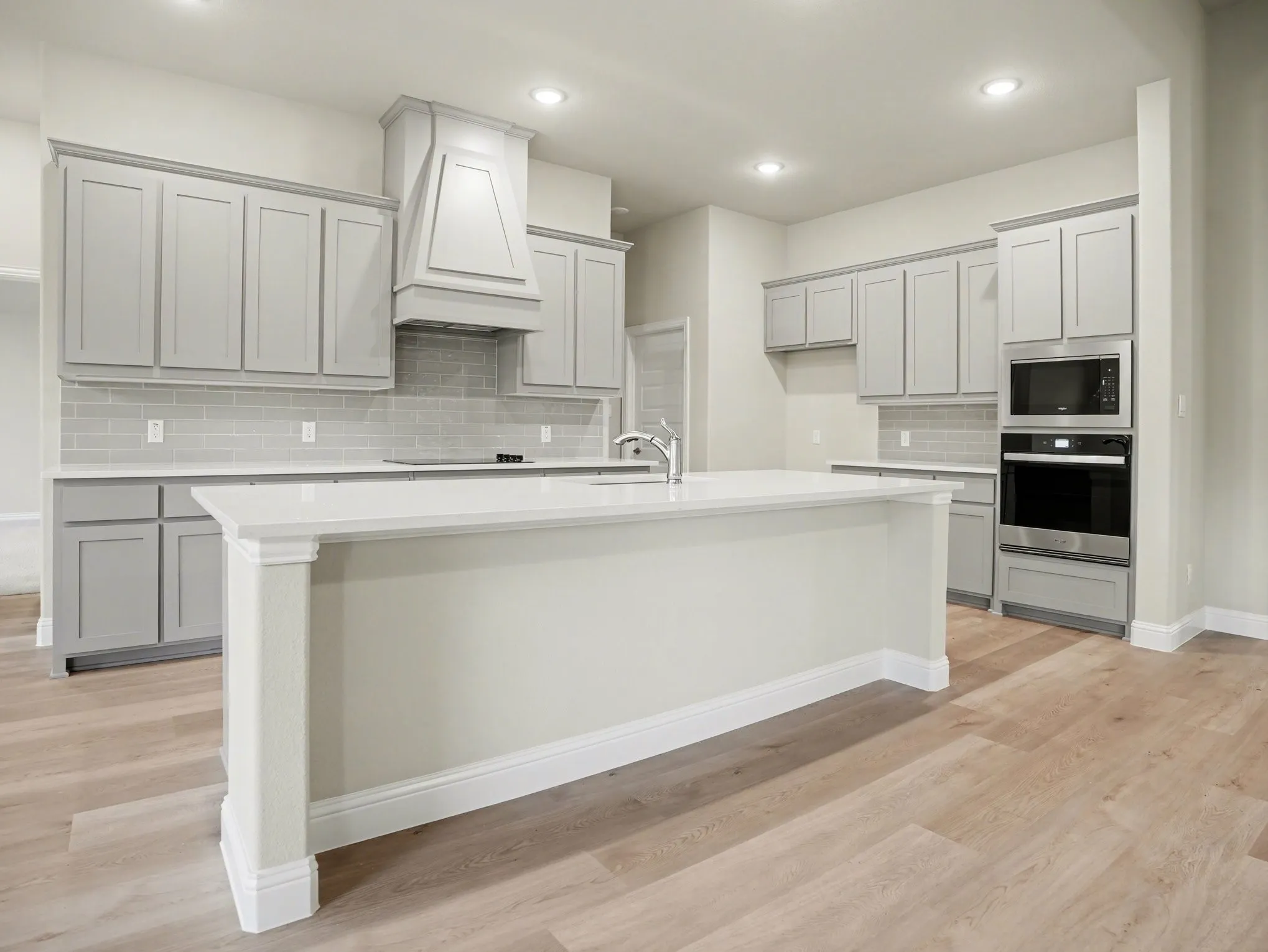 Kitchen featuring a central island with white countertop, light gray cabinetry, built-in stainless steel appliances, a subway tile backsplash, and light wood-finish flooring