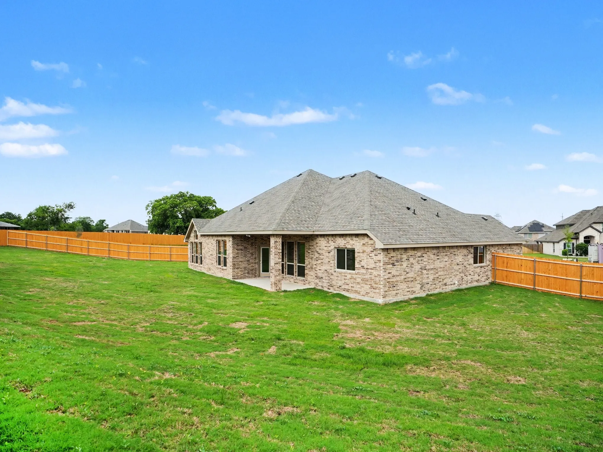 Spacious backyard with a vibrant green lawn, brick exterior, covered patio, dark-framed windows, and a wood privacy fence