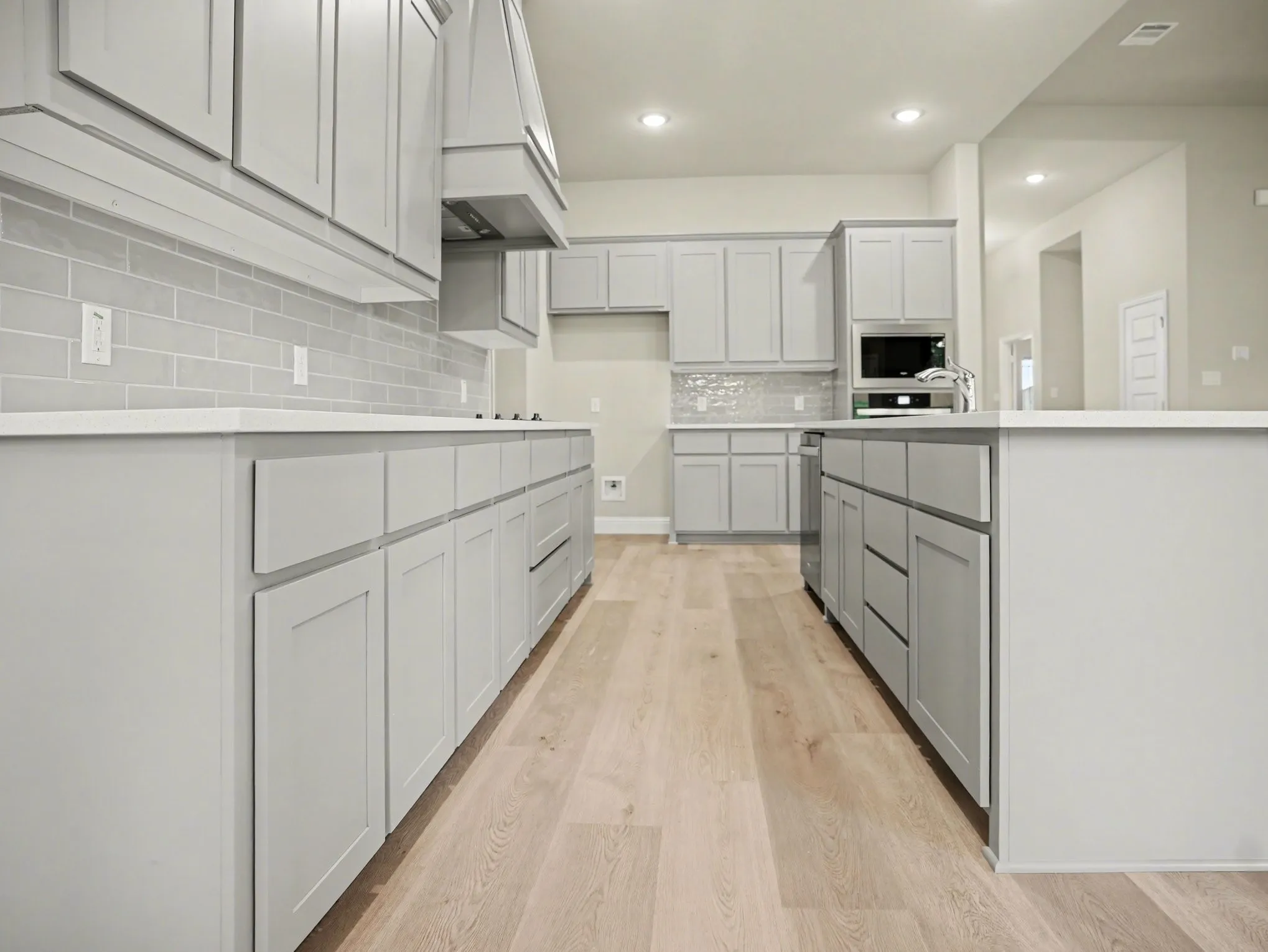 Contemporary kitchen featuring light gray shaker cabinetry, white countertops, a subway tile backsplash, and light wood-finish flooring
