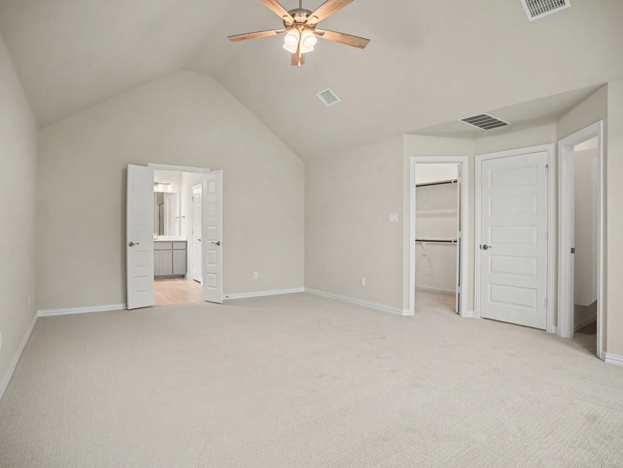 Spacious room featuring vaulted ceilings, light-toned carpeting, a ceiling fan with integrated lighting, and multiple access points including a double door entry to a bathroom and a closet with built-in shelving