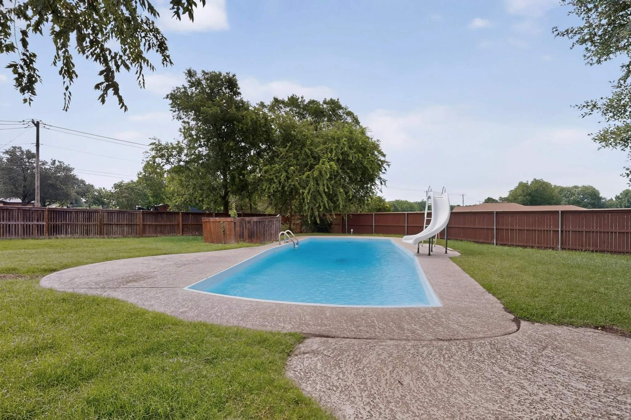 Rectangular in-ground swimming pool with a white slide and ladder, surrounded by a concrete patio