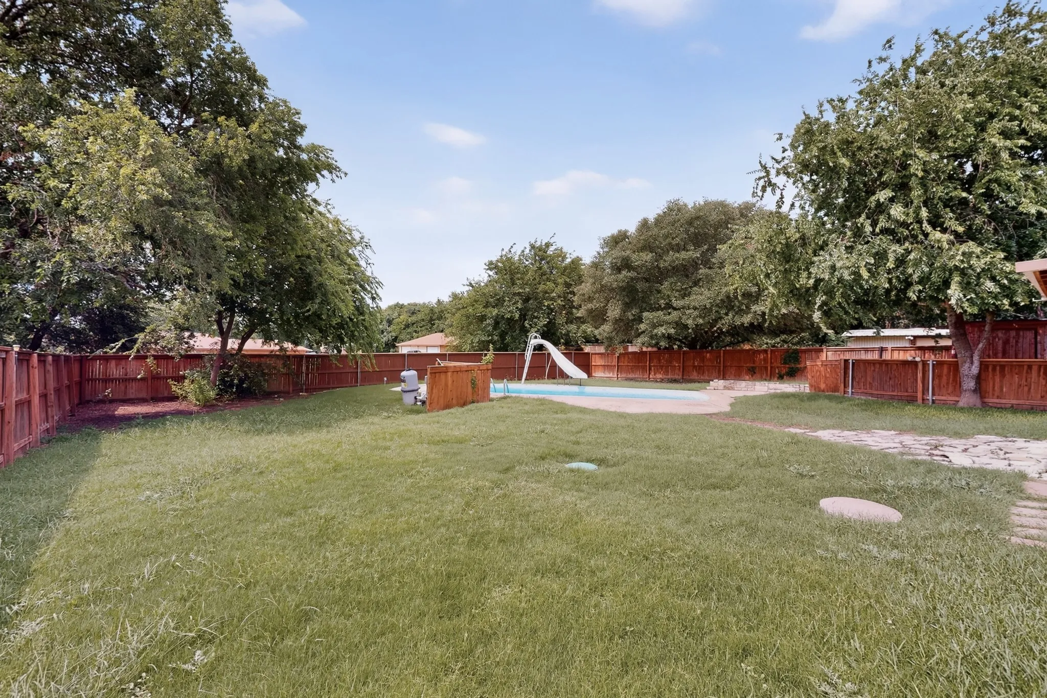 Spacious backyard featuring a rectangular swimming pool with a slide, surrounded by a wood privacy fence