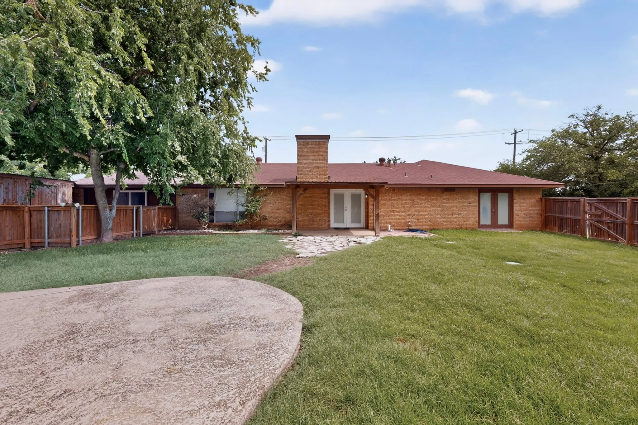 Spacious backyard featuring a large grass lawn, mature trees, and a stamped concrete patio