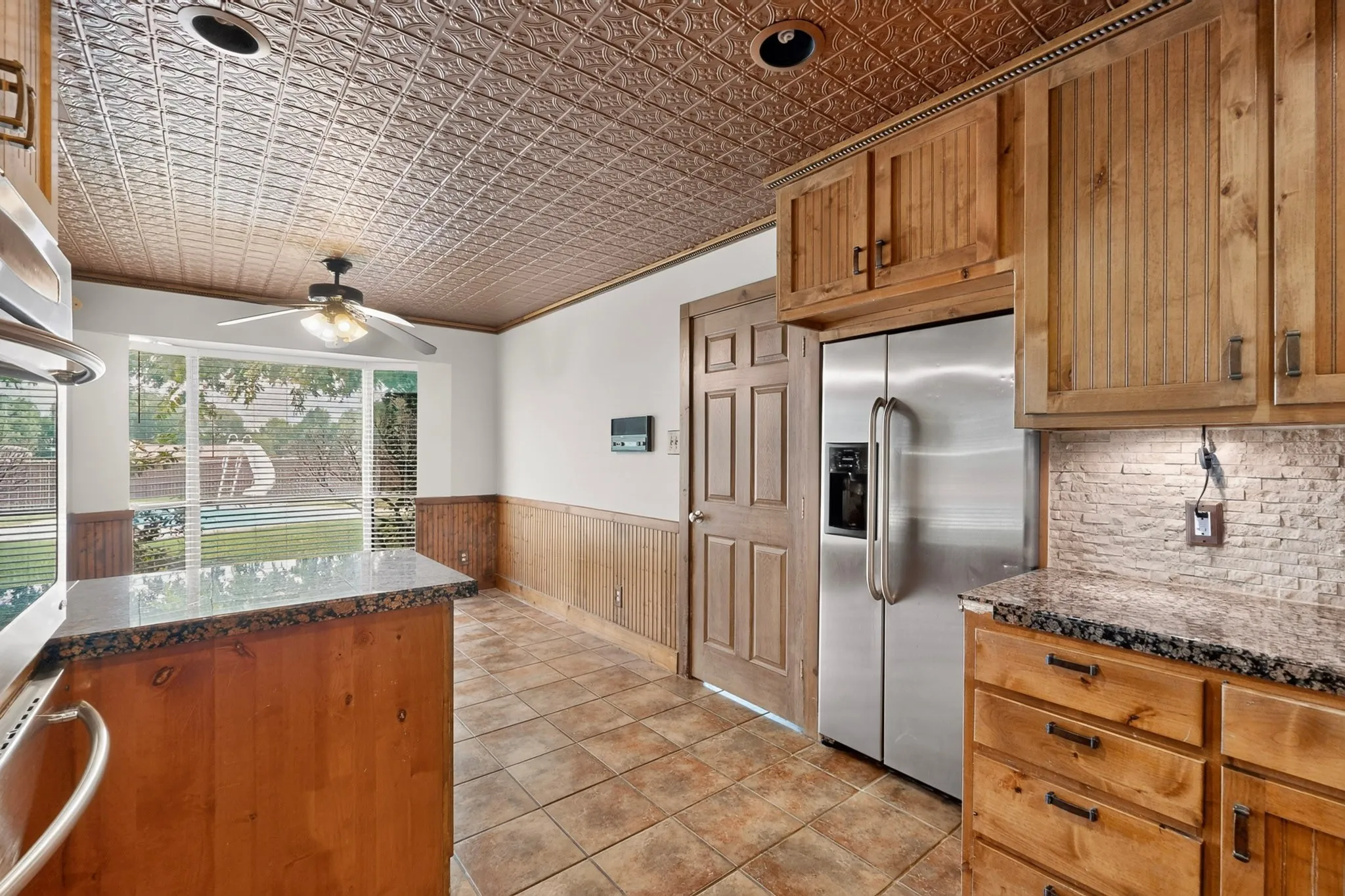 Kitchen featuring a tin-tile ceiling, wood-finish cabinetry, granite countertops, tile flooring, and a stainless steel side-by-side refrigerator