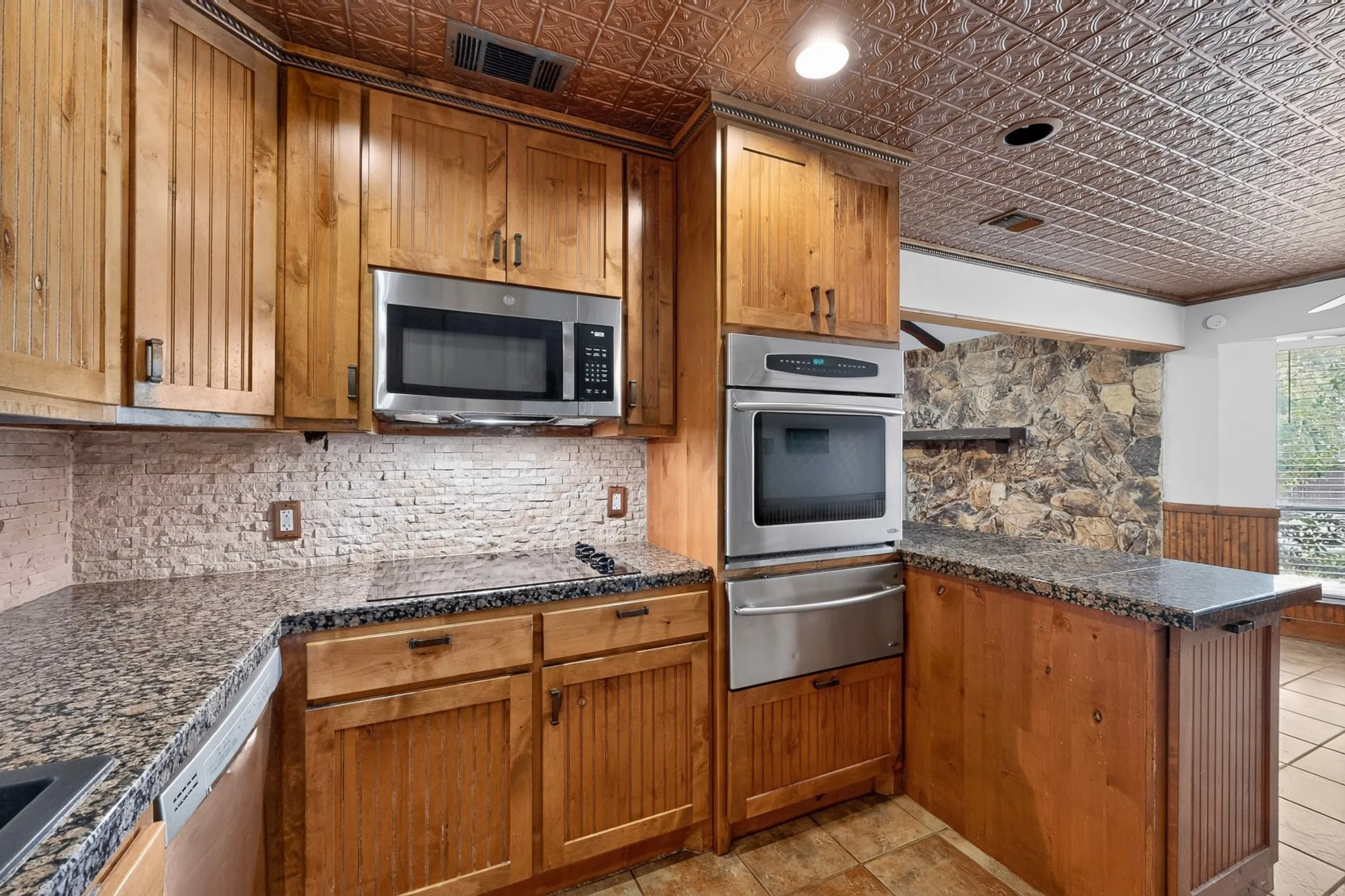 Kitchen featuring natural wood cabinetry, granite countertops, a built-in stainless steel microwave, and a double oven