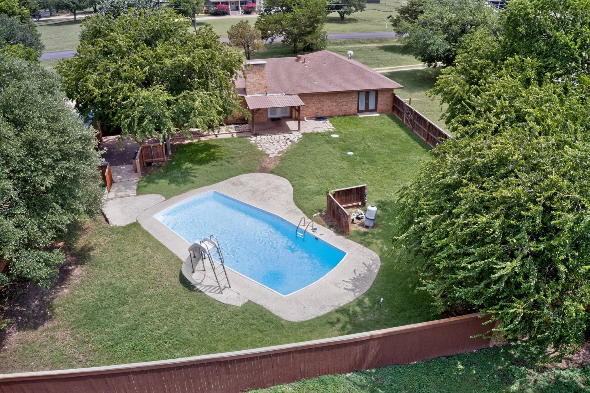 Expansive backyard featuring a large swimming pool with concrete surround, manicured lawn, and mature trees providing natural privacy