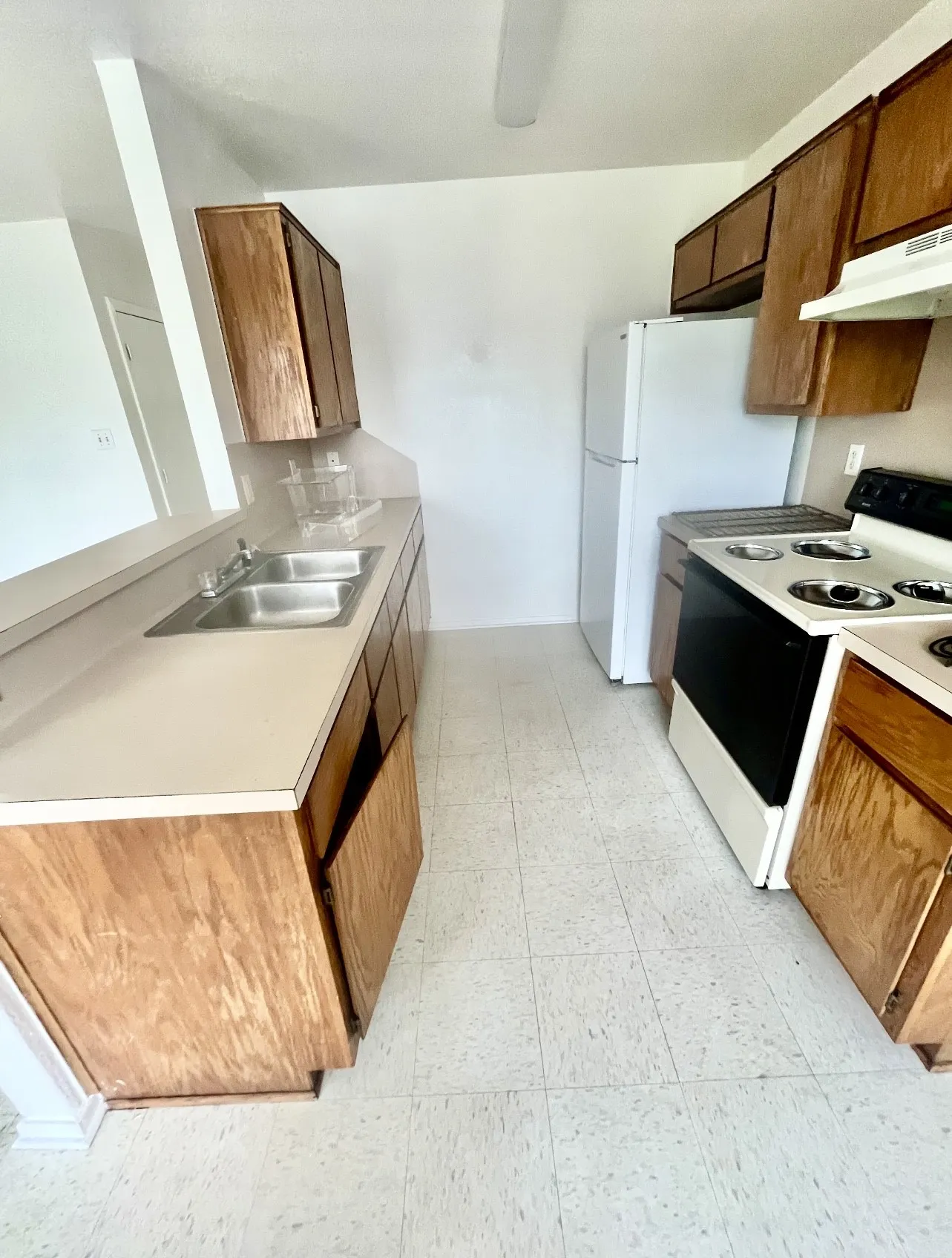 Kitchen with white range with electric stovetop, light countertops, brown cabinetry, under cabinet range hood, and light flooring