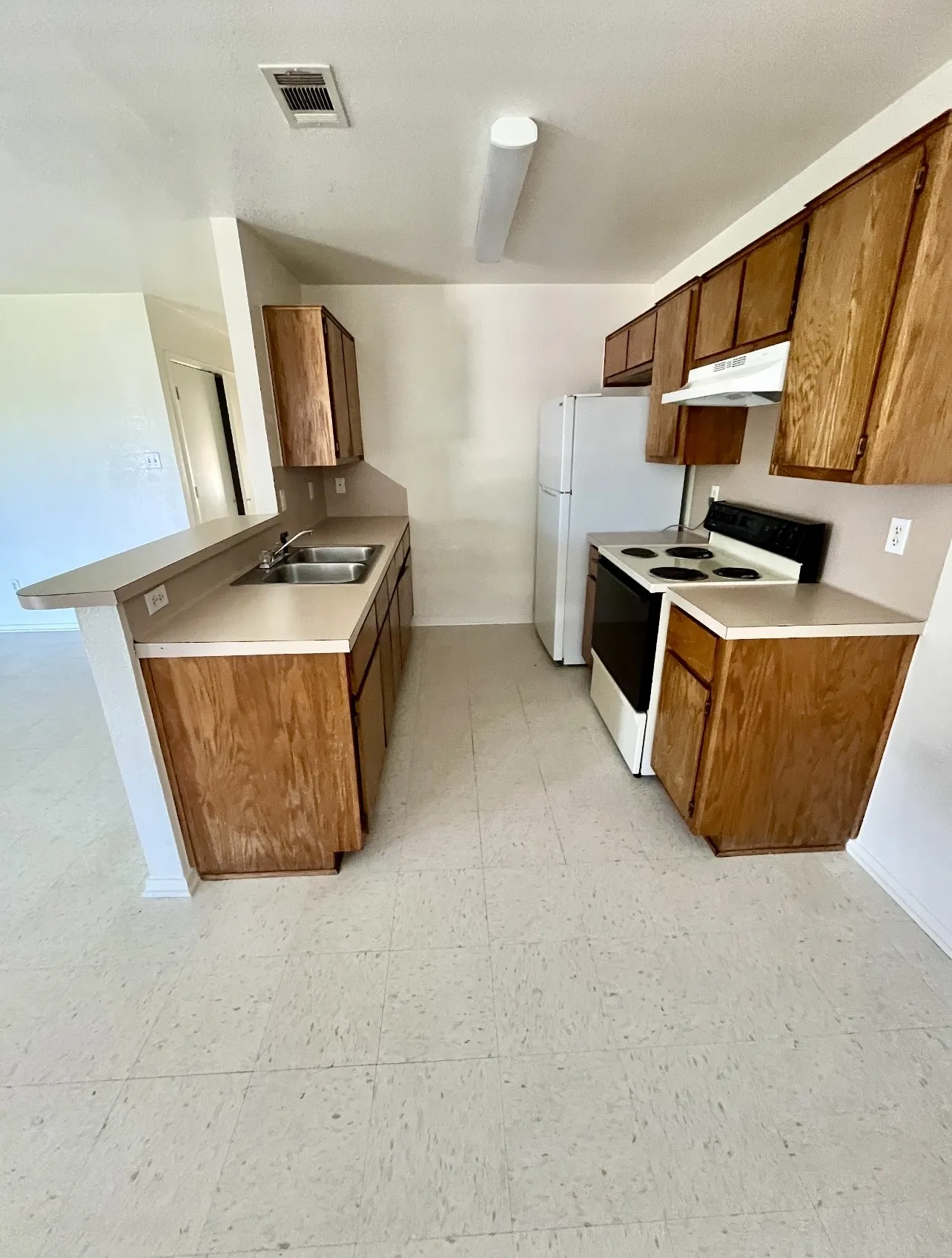 Kitchen featuring white electric range oven, brown cabinetry, a peninsula, light countertops, and light floors