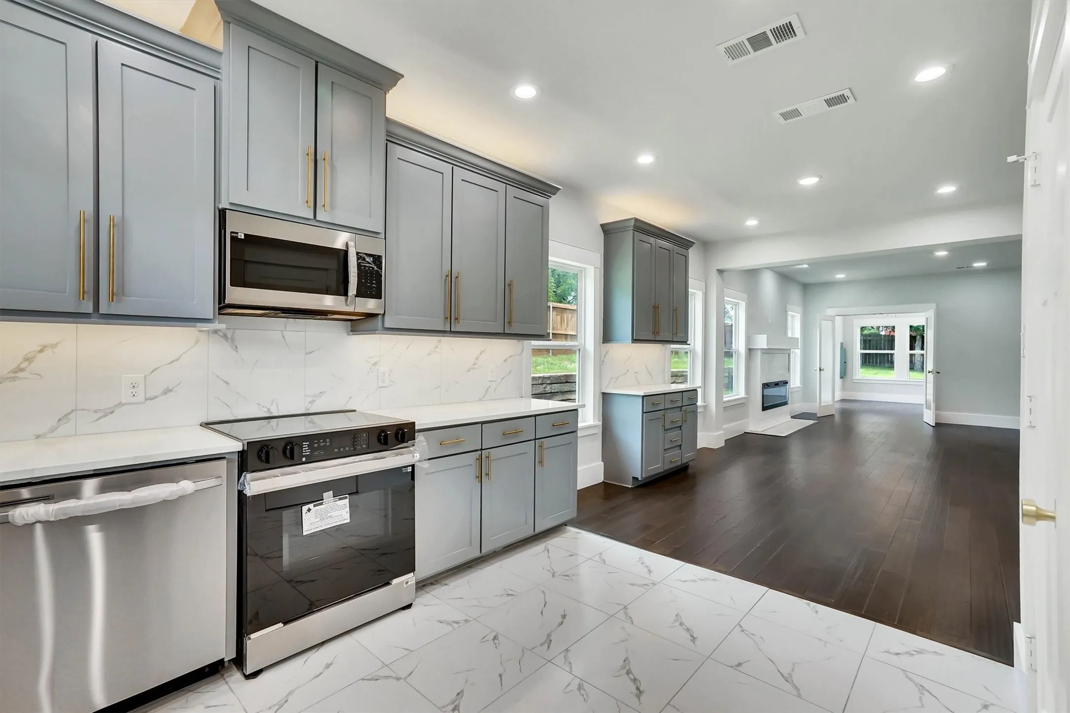 Modern kitchen featuring stainless steel appliances, light gray cabinetry with gold-tone hardware, quartz countertops, and a white tile backsplash