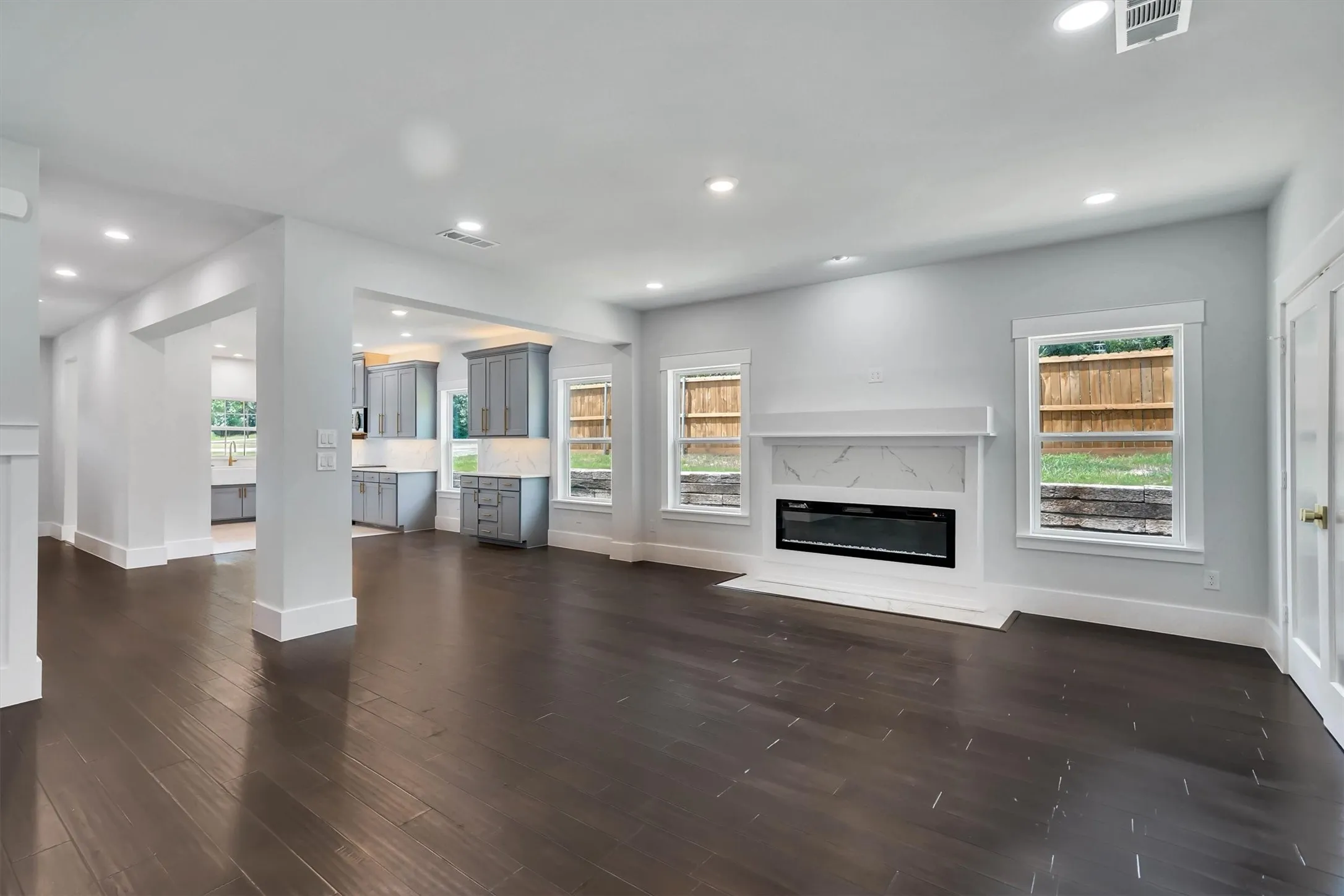 Spacious interior with dark wood-finish flooring, recessed lighting, and a modern fireplace featuring a white mantel and marble-patterned surround