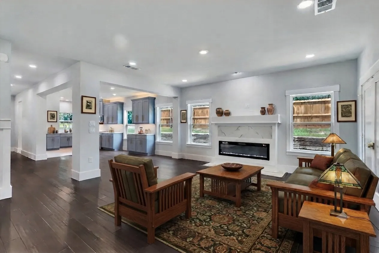 Spacious open-concept living area featuring dark wood-finish flooring, recessed lighting, and a modern fireplace with a white surround and mantel