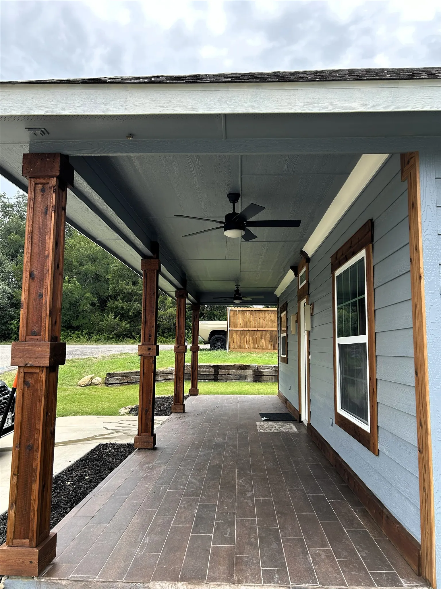 Expansive covered porch featuring tiled wood-like finish flooring, substantial cedar wood-clad support columns, and multiple ceiling fans
