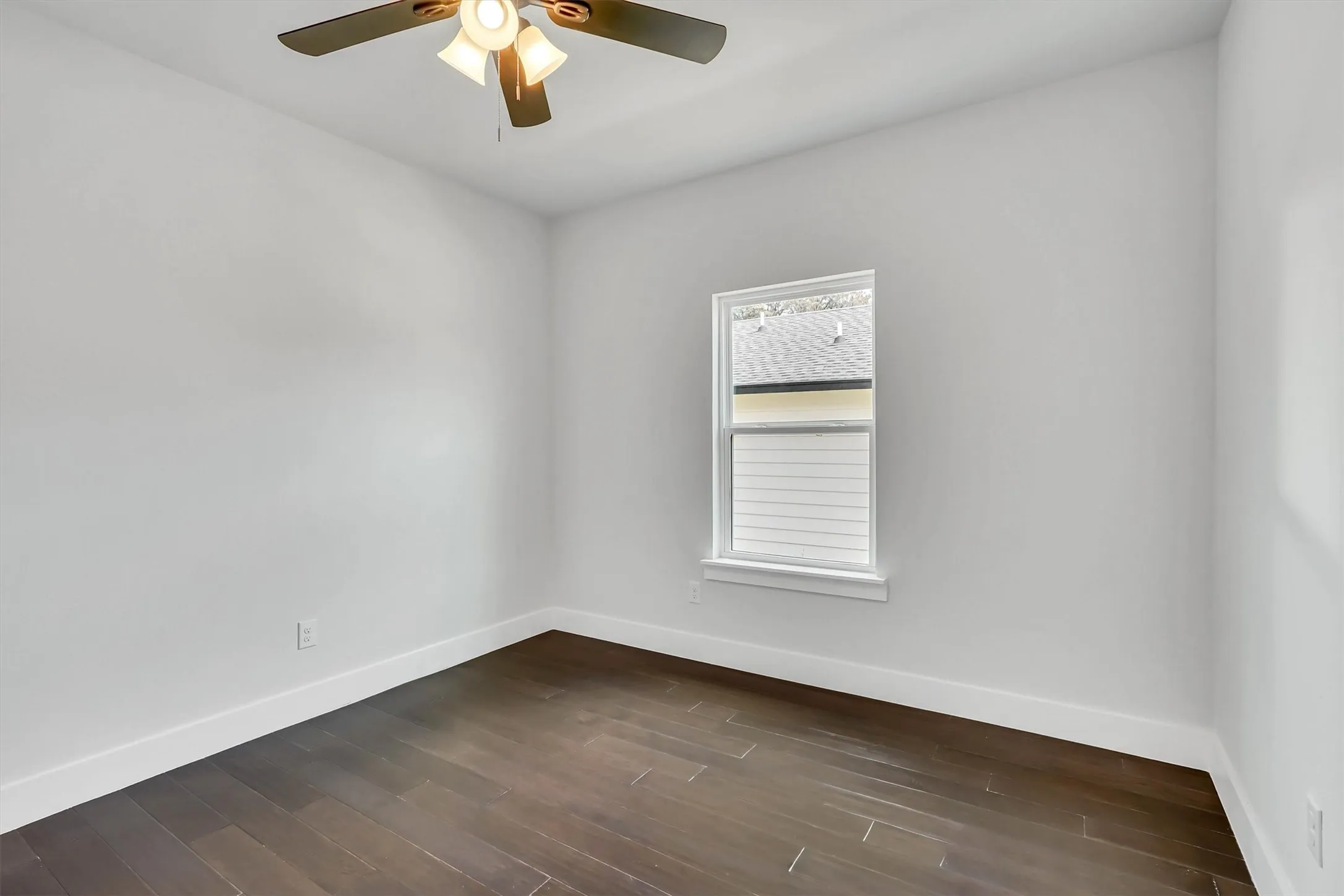 Contemporary room featuring wood-finish flooring, white baseboards, a ceiling fan with integrated lighting, and a double-hung window