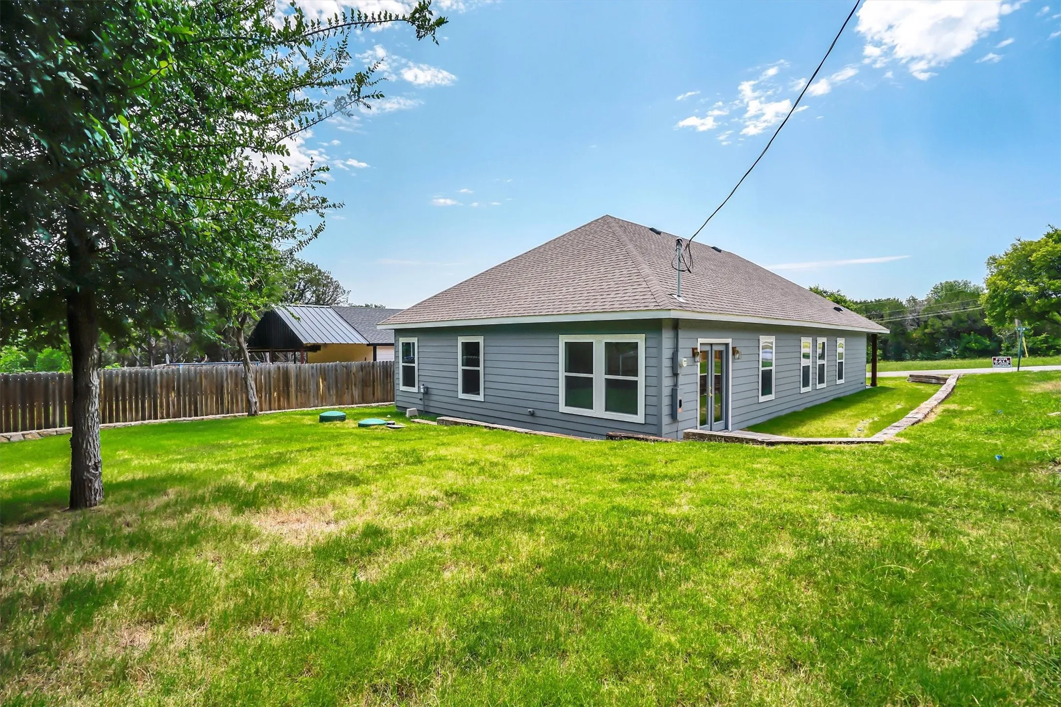 Spacious exterior featuring gray horizontal siding, a gabled roof, multiple white-framed windows, and an outdoor patio with a covered entry