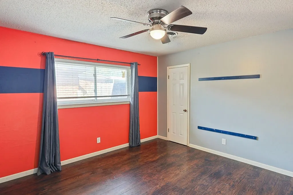 Spacious room featuring wood-finish flooring, a ceiling fan with integrated lighting, and a white paneled door