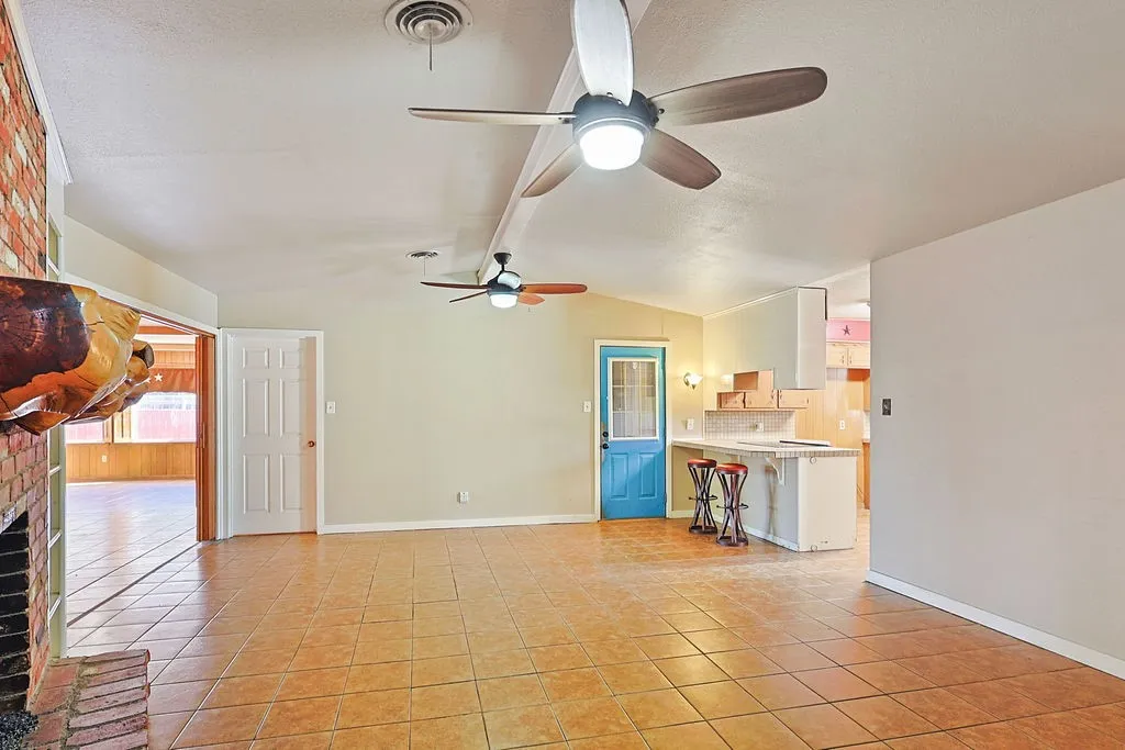 Spacious living area featuring tile flooring, a brick fireplace with a wood mantel, and multiple ceiling fans