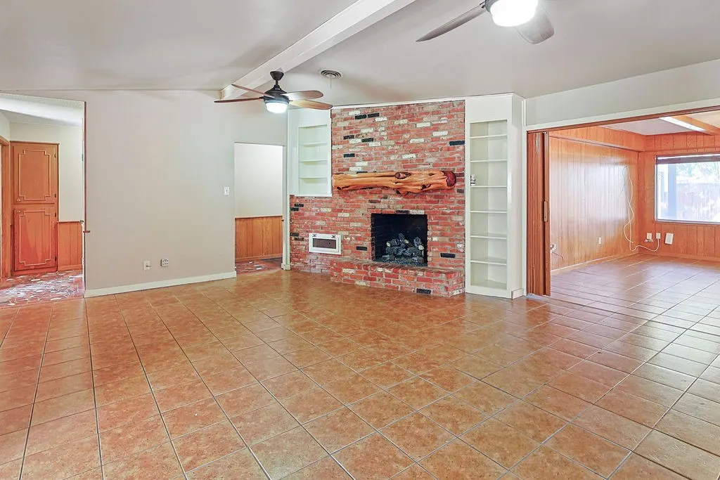 Living area featuring tile flooring, a brick fireplace with a wood mantel, and built-in shelving