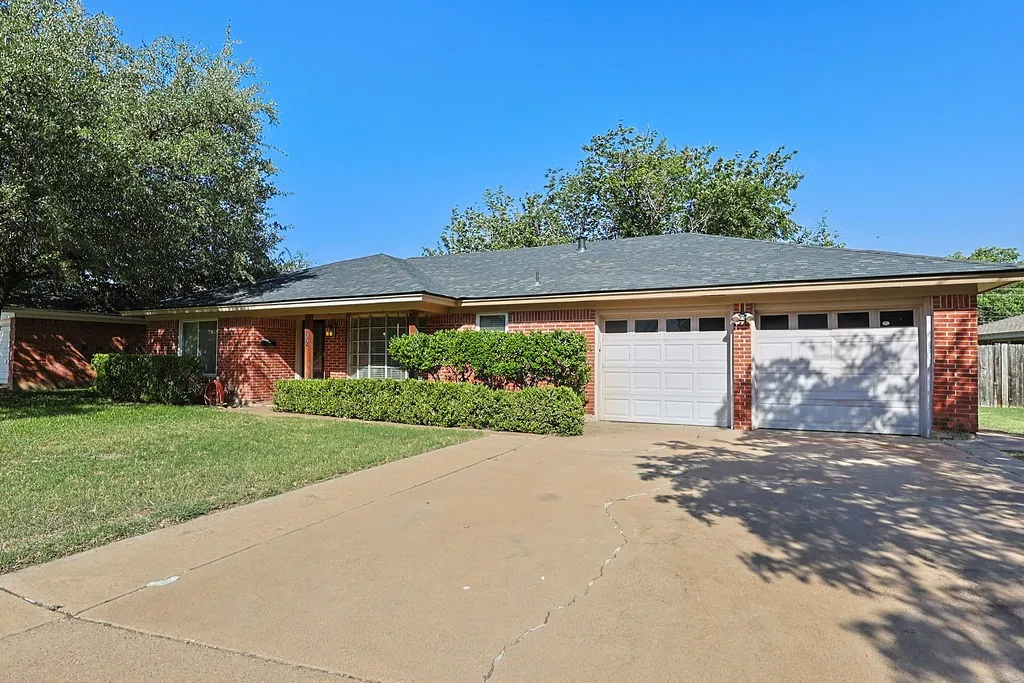 Traditional brick residence with a two-car garage, mature front yard landscaping, and a concrete driveway