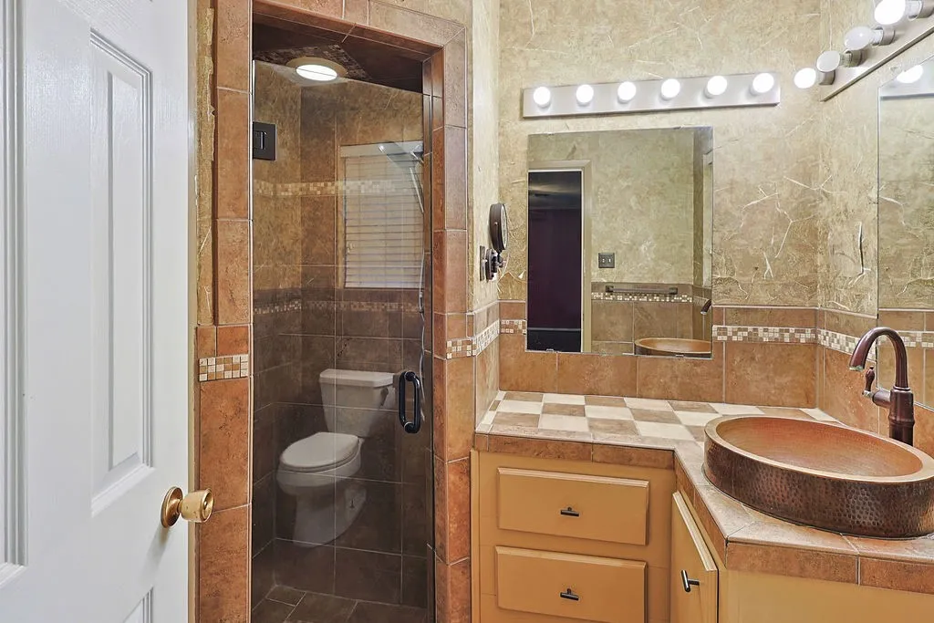 Full bathroom featuring a walk-in shower with clear glass enclosure and tiled walls, a vanity with a copper vessel sink, and a large wall-mounted mirror