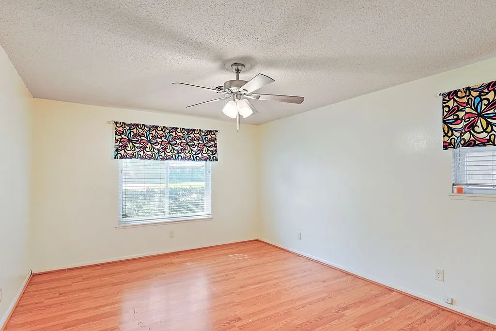 Room featuring wood-finish flooring, two windows with horizontal blinds, and a ceiling fan with integrated lighting