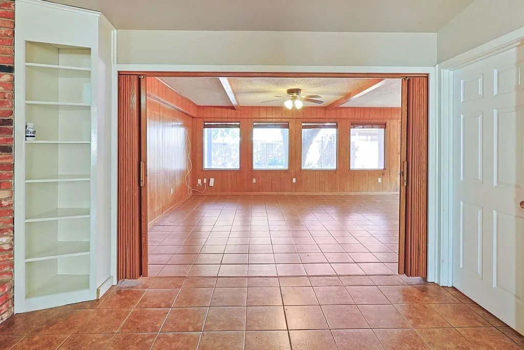 Spacious room featuring tile flooring, wood-paneled walls, multiple windows, and a ceiling fan