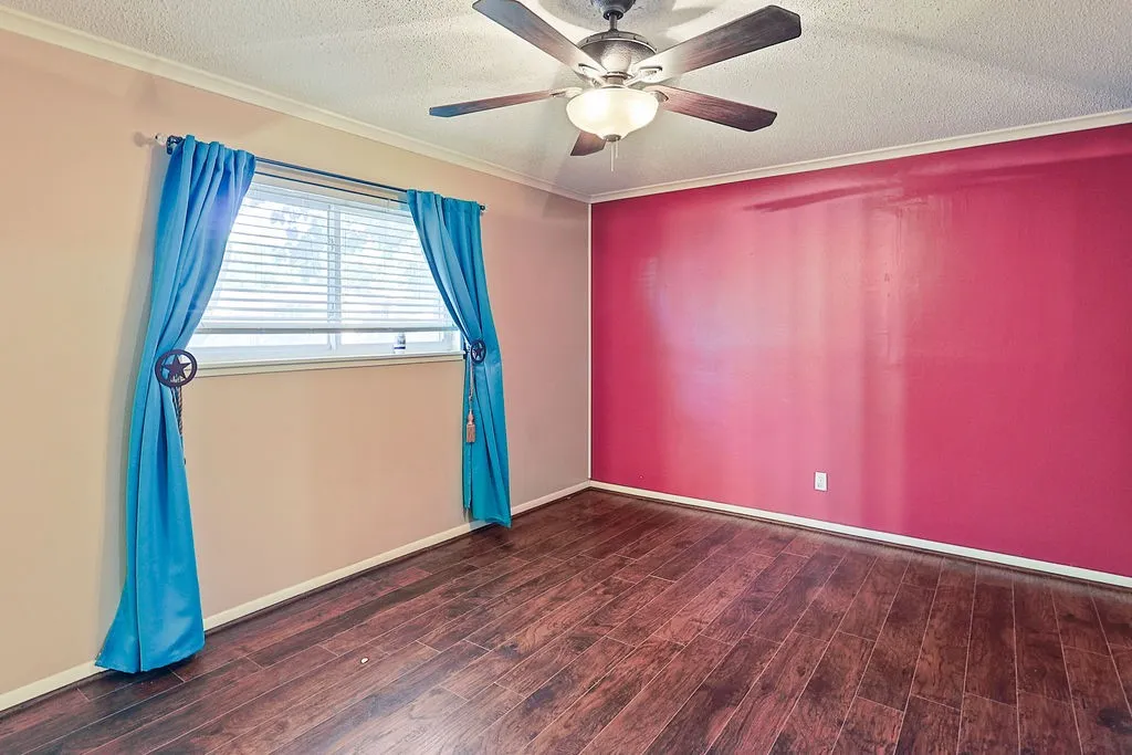 Spacious room featuring rich wood-finish flooring and a ceiling fan with integrated lighting