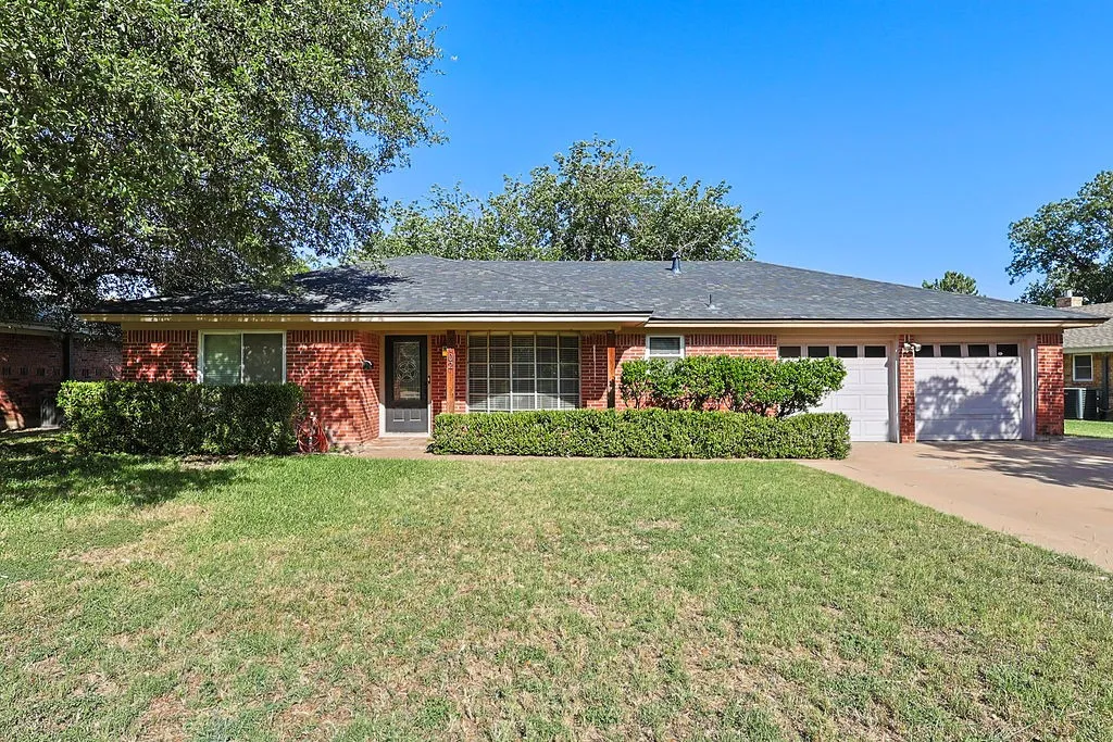 Red brick exterior featuring a dark entry door, two-car garage, and mature landscaping
