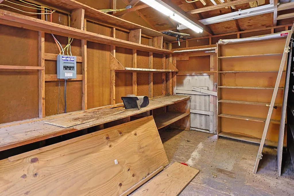 Utility space featuring exposed wood framing, built-in shelving, a workbench, and a visible electrical panel