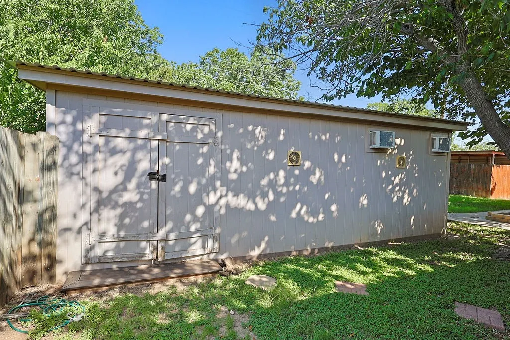 Detached outbuilding featuring a metal roof, double entry doors, two wall-mounted HVAC units, and two circular vents