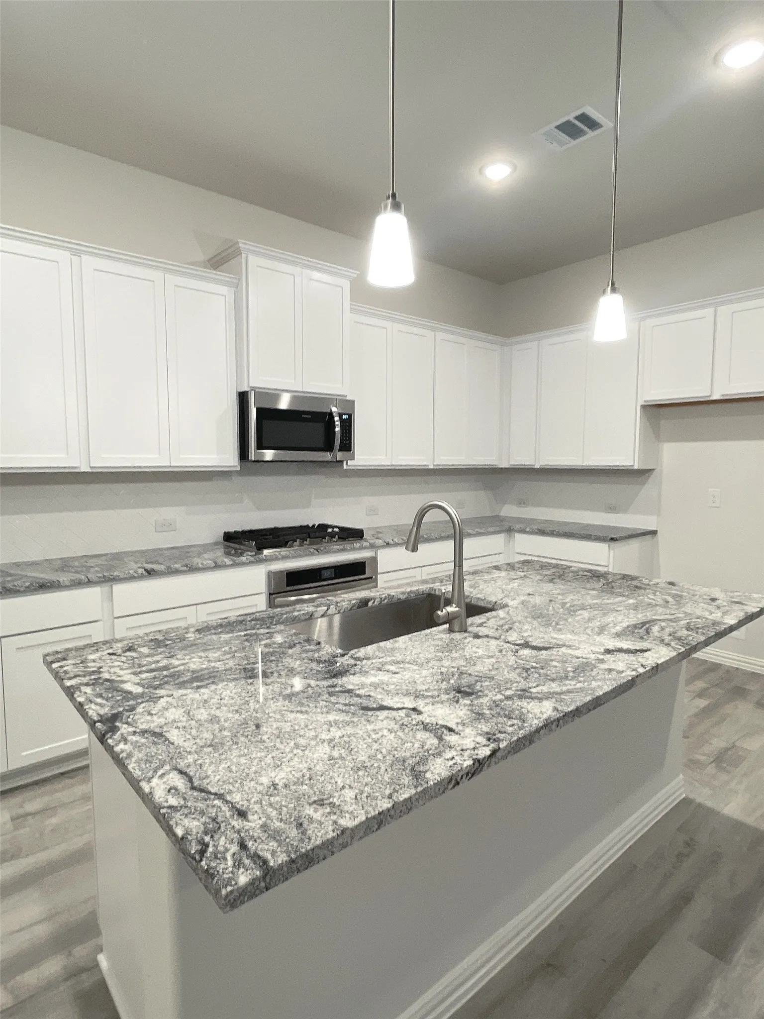 Kitchen with stainless steel appliances, white cabinetry, visible vents, and decorative light fixtures