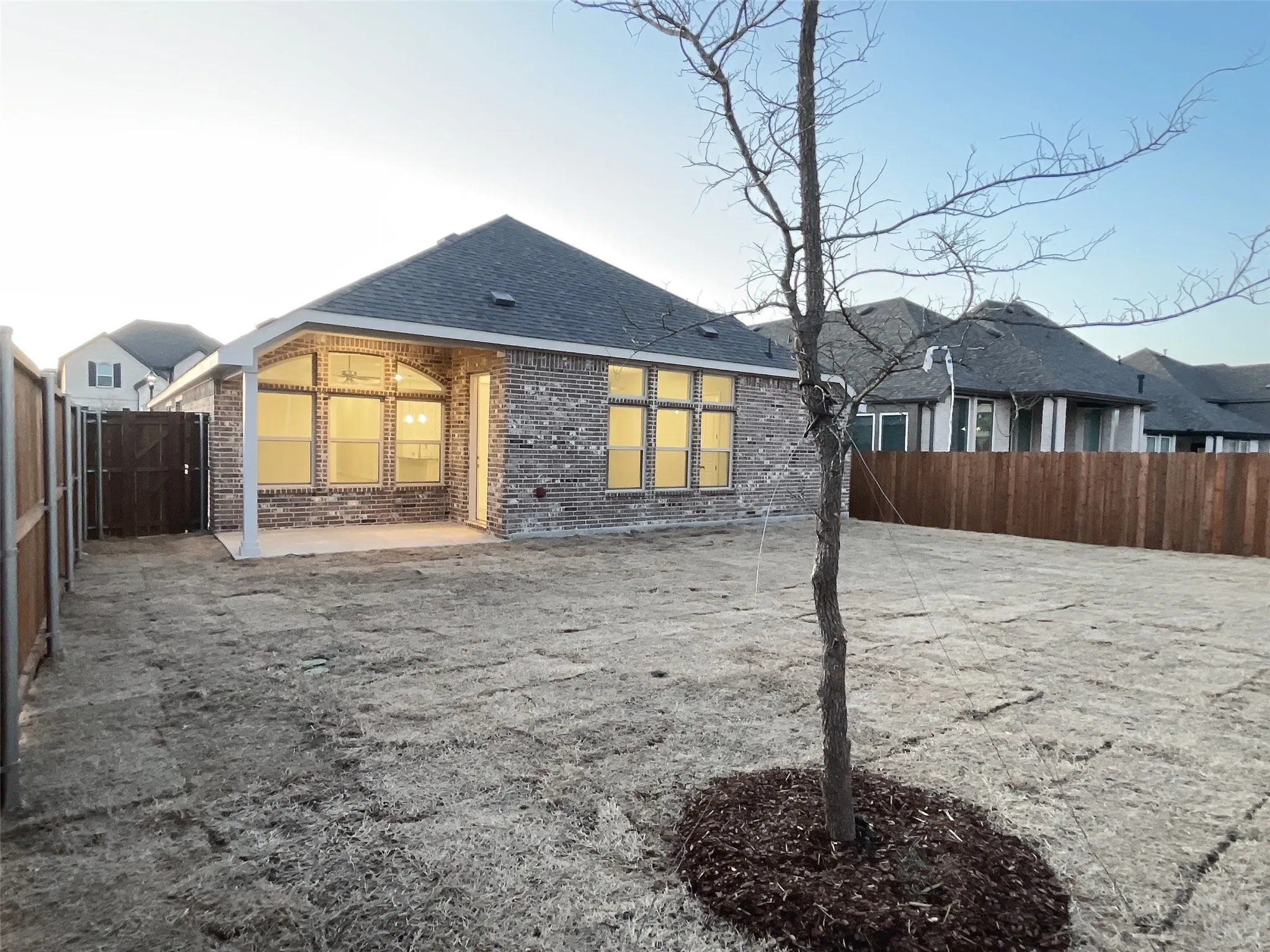Back of house with a patio, brick siding, roof with shingles, and a fenced backyard