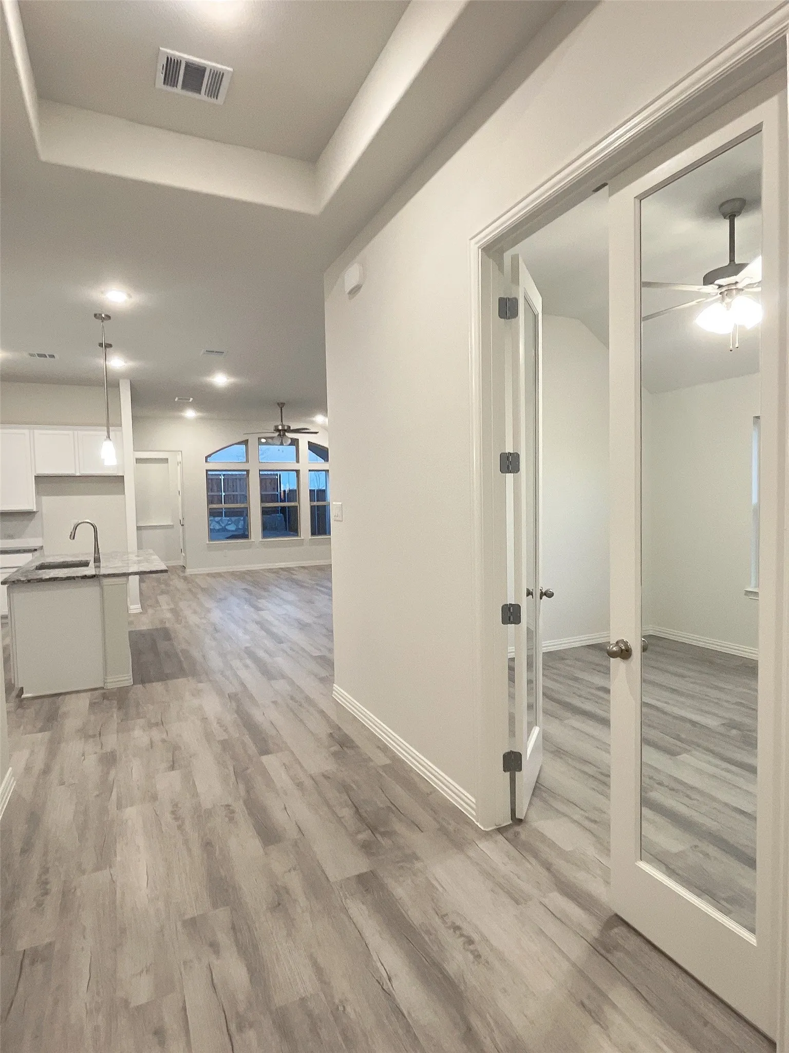Hall featuring light wood-style floors, visible vents, a raised ceiling, and a sink