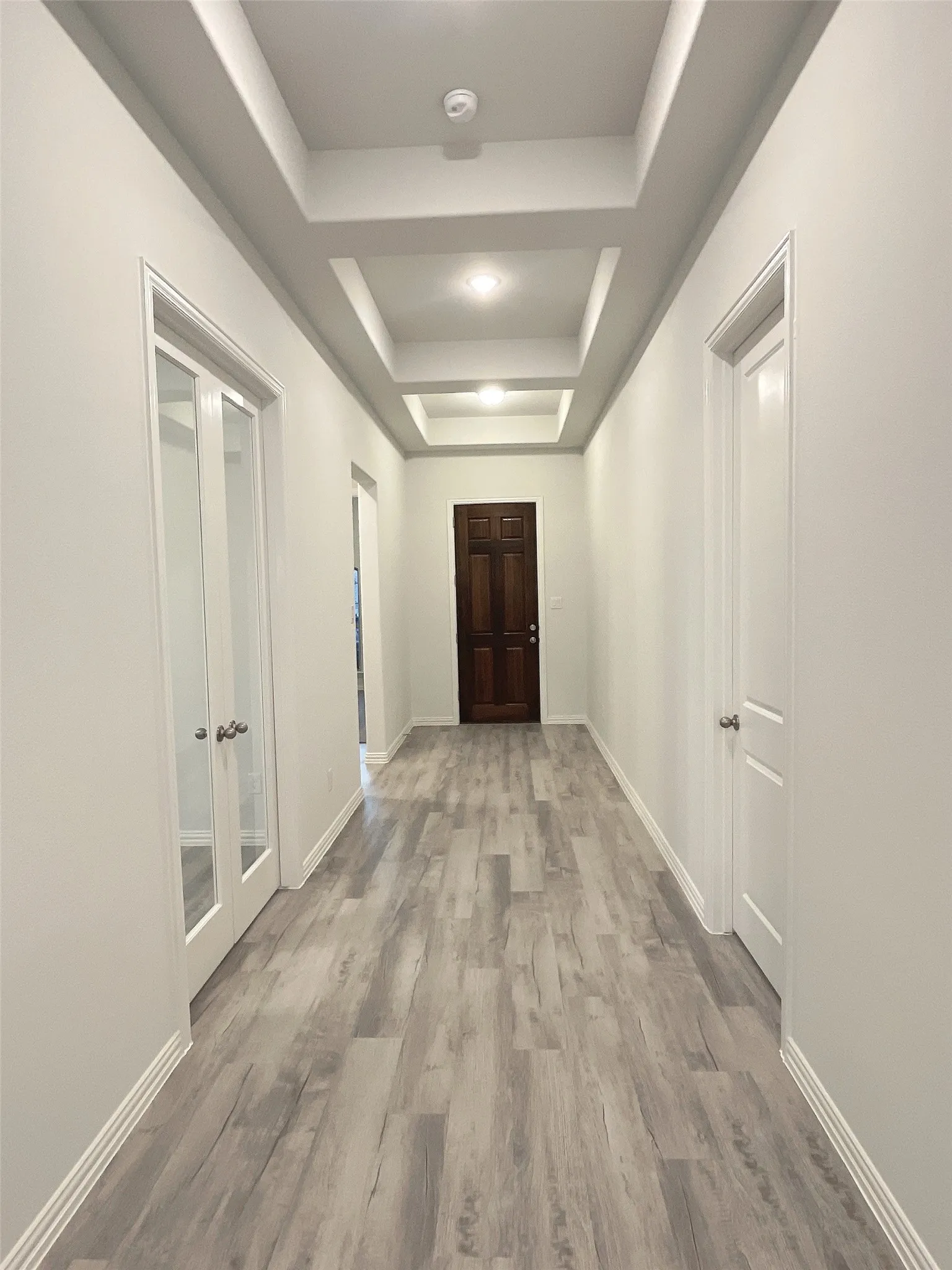 Hallway featuring light wood-style floors, baseboards, and a raised ceiling