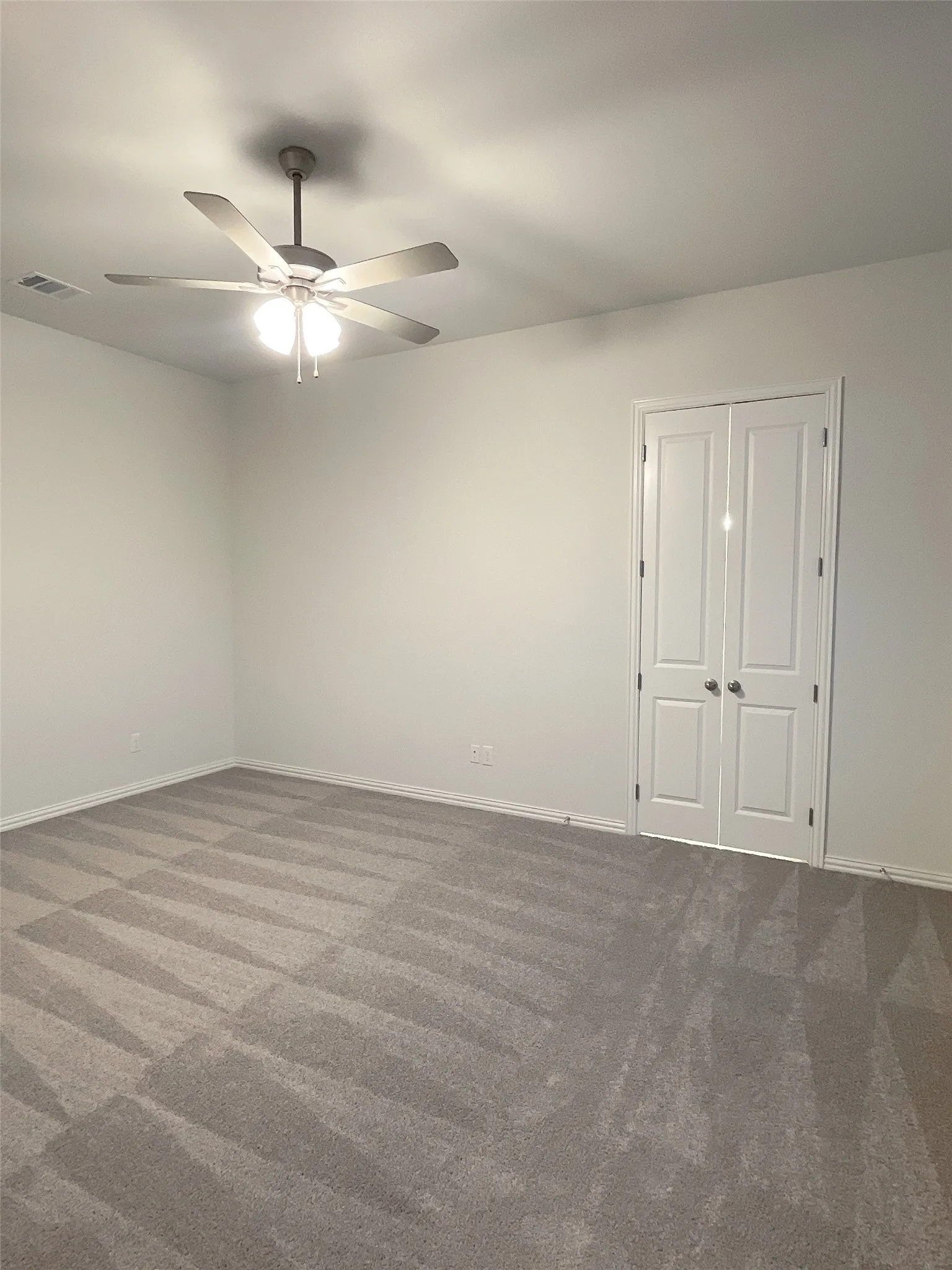 Empty room featuring carpet flooring, ceiling fan, visible vents, and baseboards