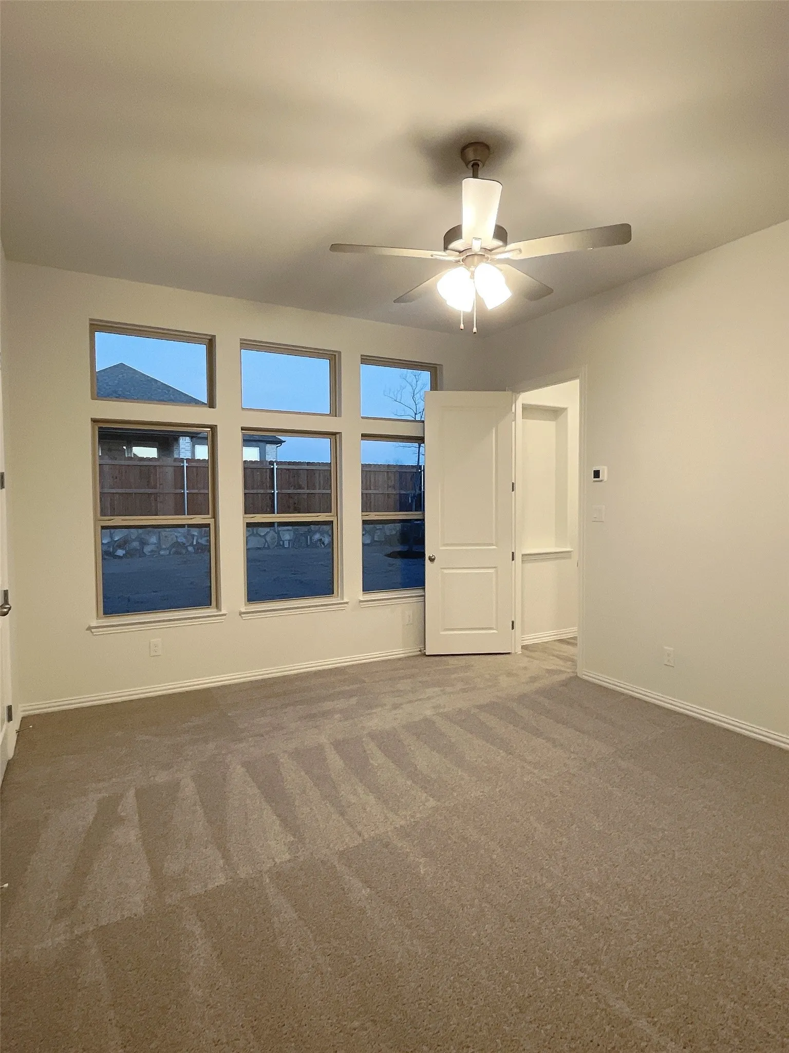 Carpeted empty room featuring ceiling fan and baseboards