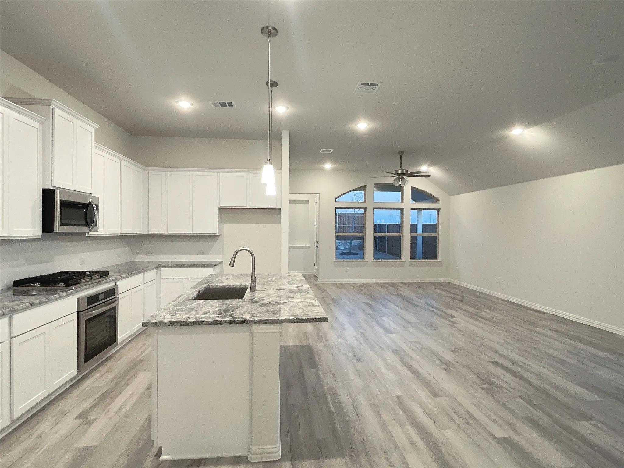 Kitchen with an island with sink, appliances with stainless steel finishes, open floor plan, pendant lighting, and a sink