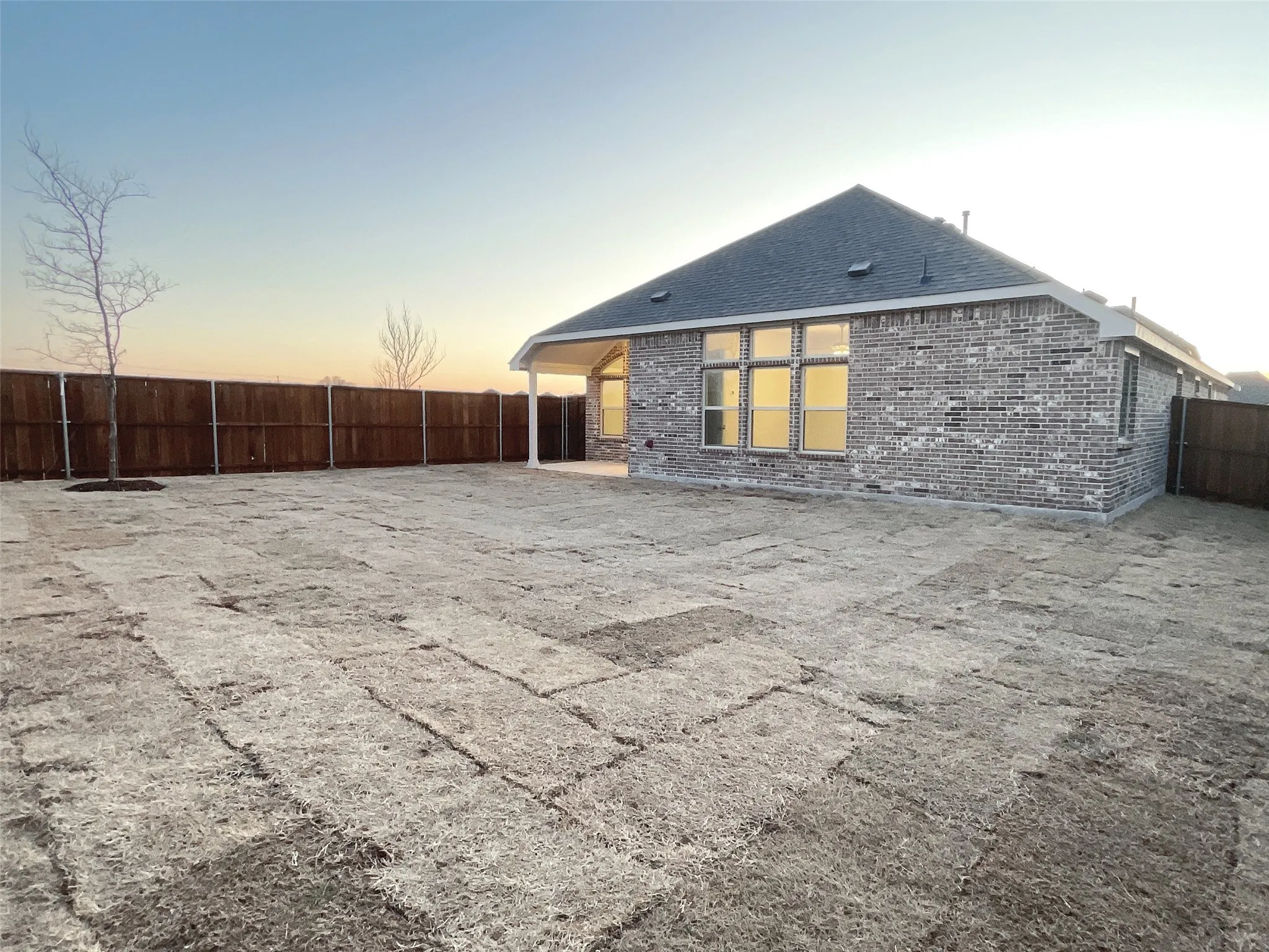 Back of property at dusk with brick siding, a fenced backyard, and roof with shingles