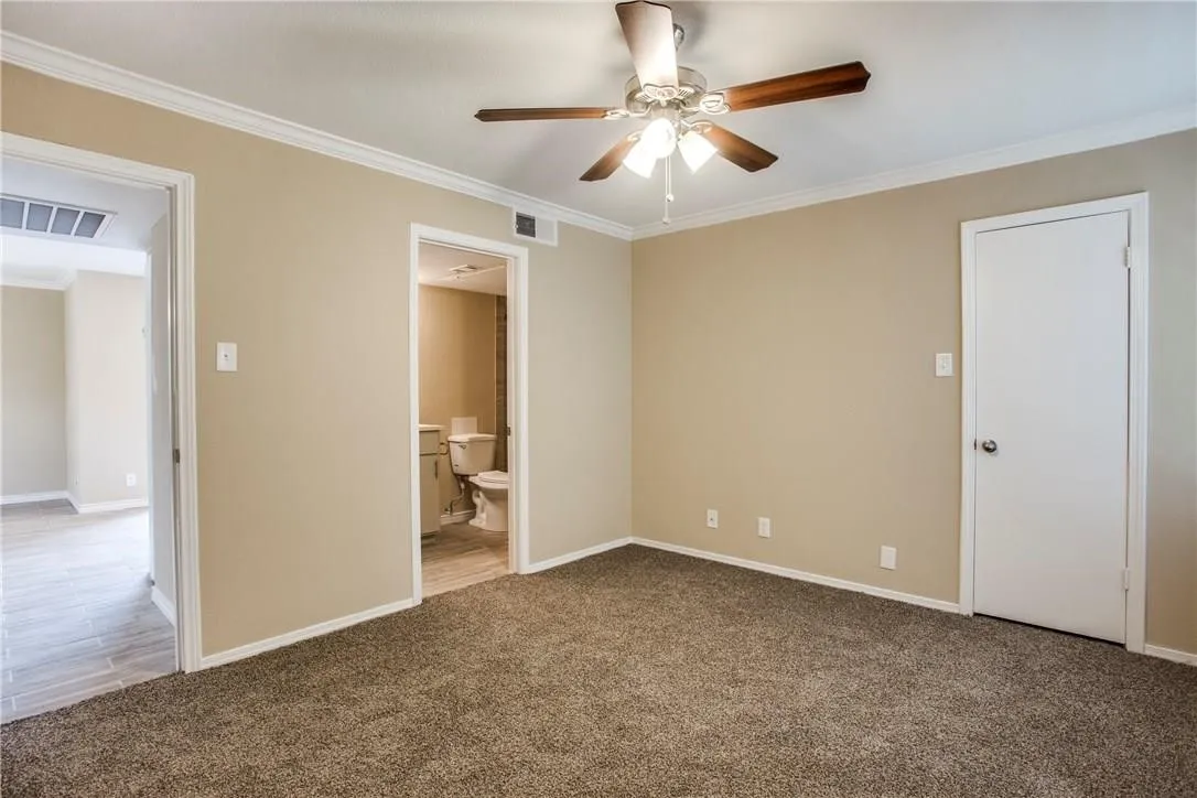 Unfurnished bedroom with ensuite bath, carpet, ceiling fan, and ornamental molding