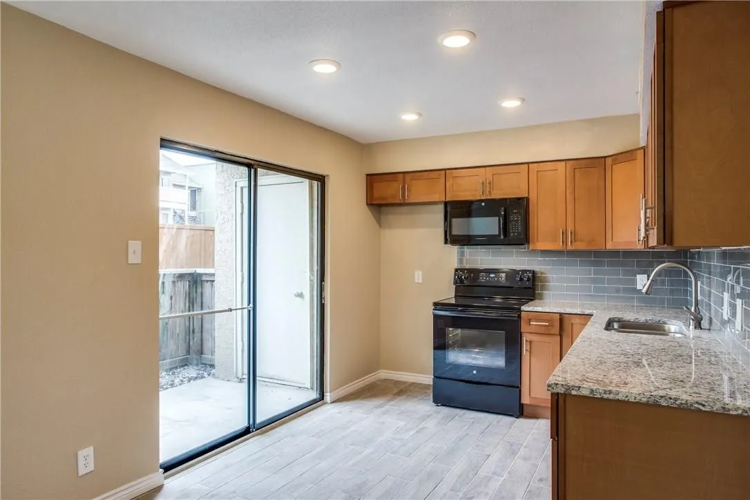 Kitchen featuring black appliances, tasteful backsplash, sink, light stone countertops, and light hardwood / wood-style floors