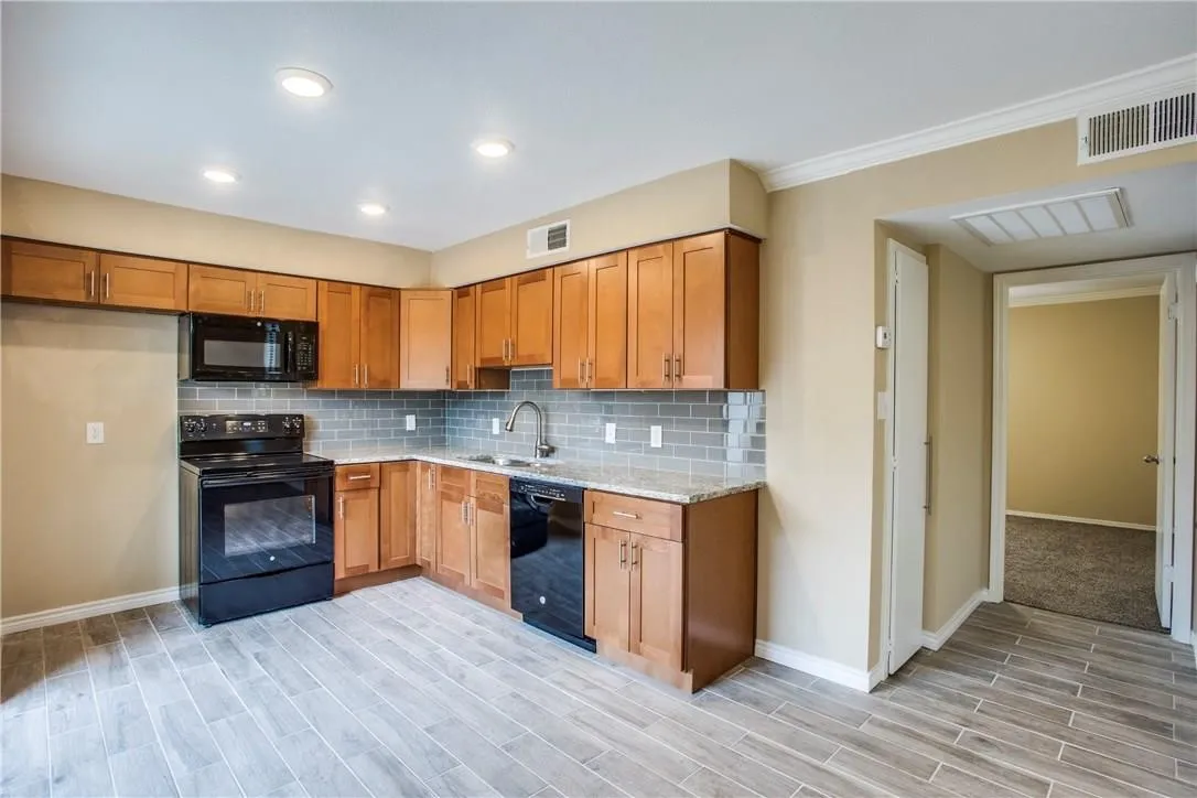 Kitchen featuring tasteful backsplash, light stone countertops, black appliances, light colored carpet, and sink