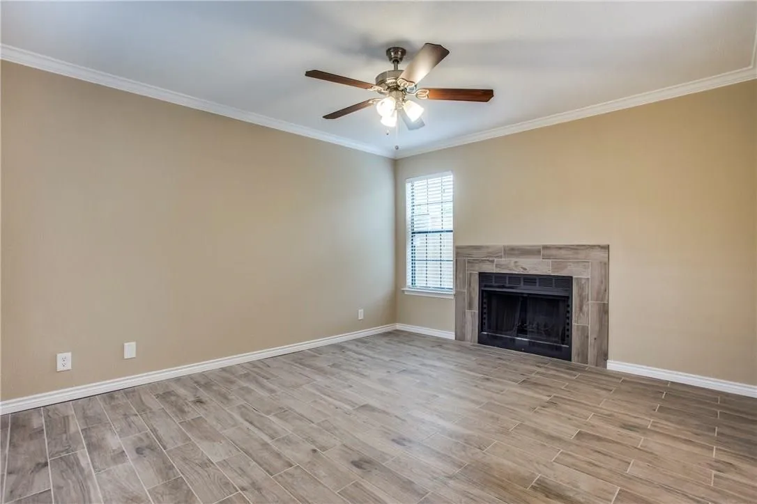 Unfurnished living room with crown molding, light hardwood / wood-style floors, a tile fireplace, and ceiling fan