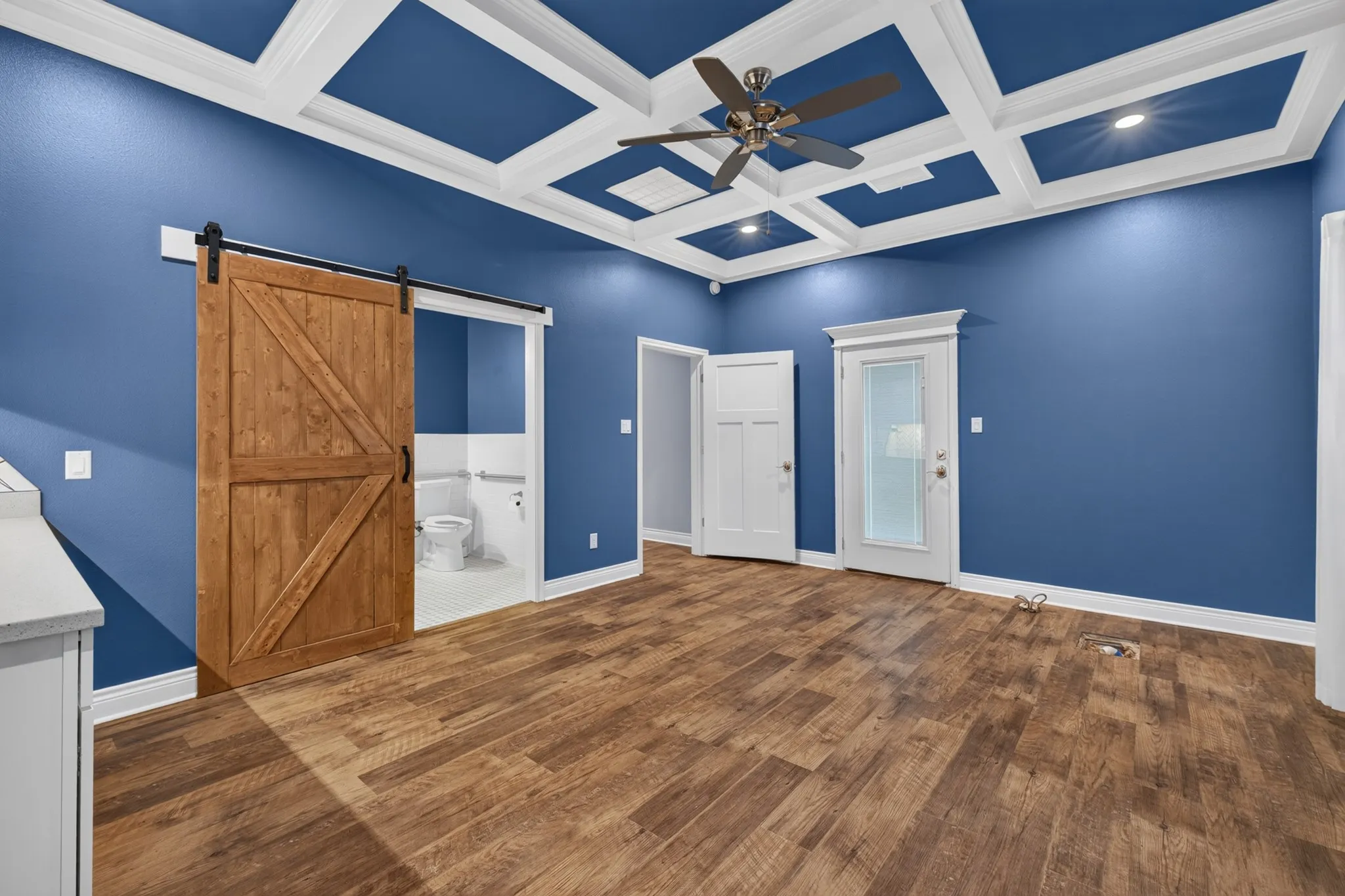 Wood-finish flooring throughout, coffered ceiling with recessed lighting and ceiling fan, and a wood barn door