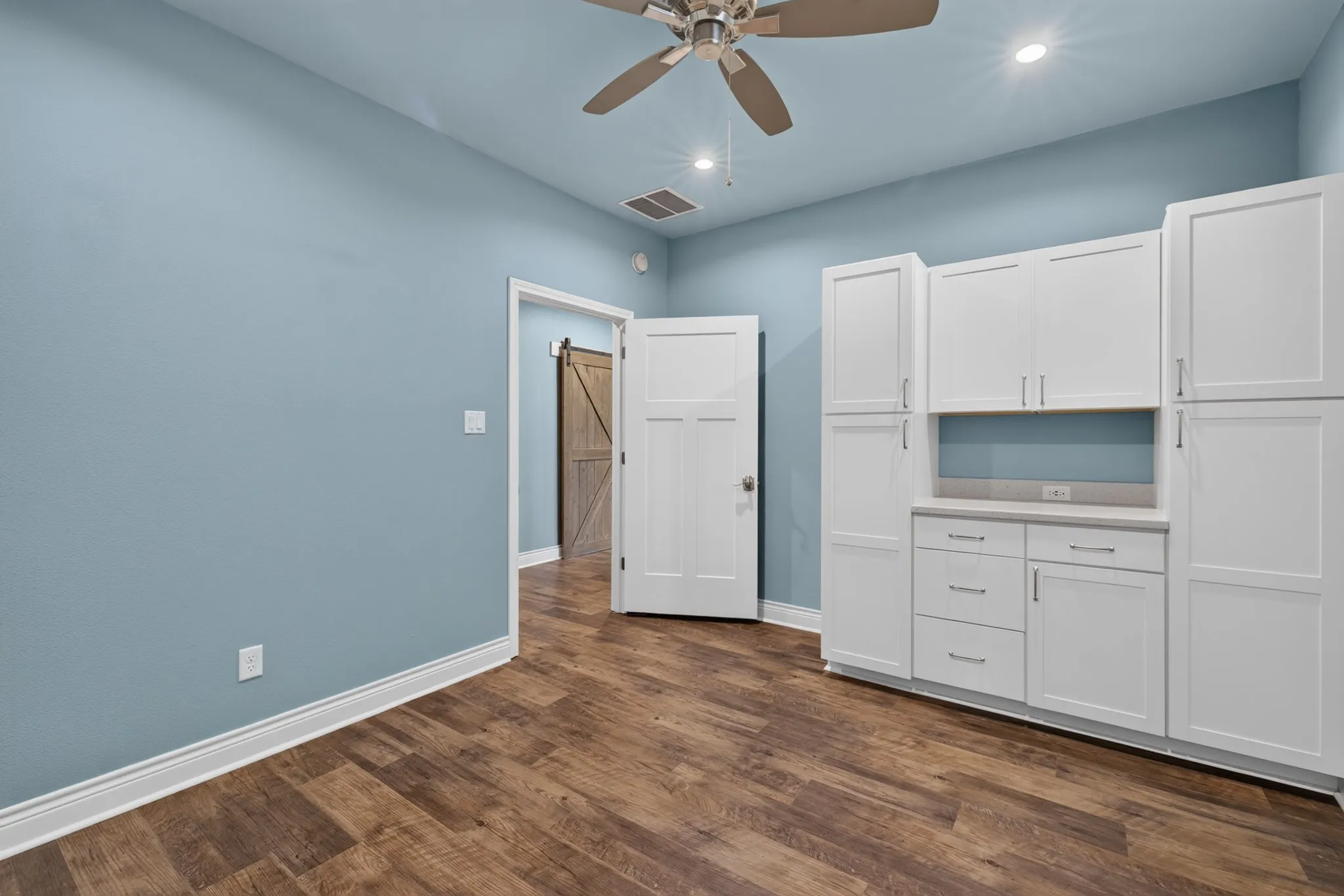 Wood-finish flooring, white built-in cabinetry, recessed lighting, and a ceiling fan