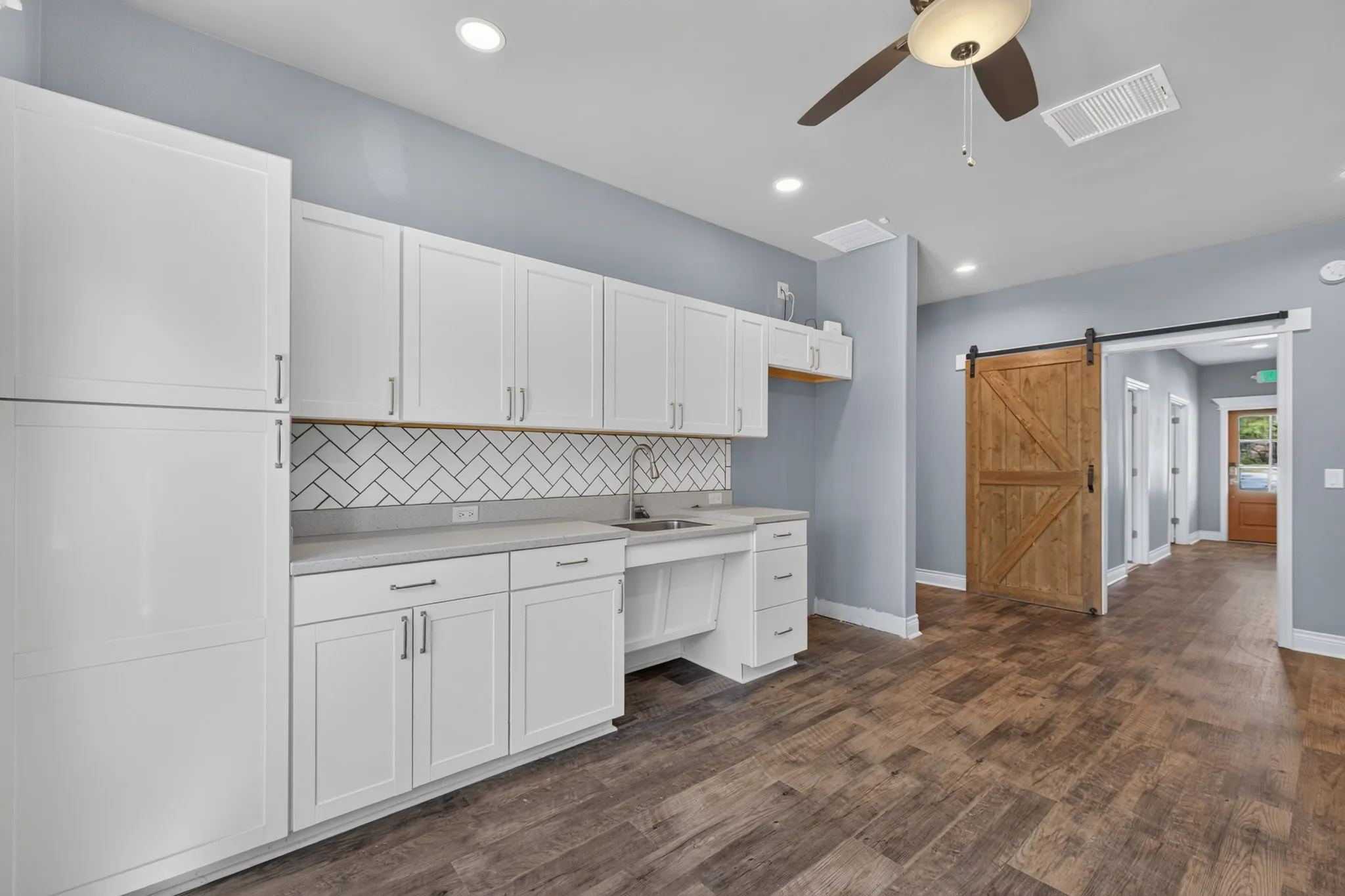 White shaker cabinetry, herringbone tile backsplash, wood-finish flooring, recessed lighting, and a ceiling fan