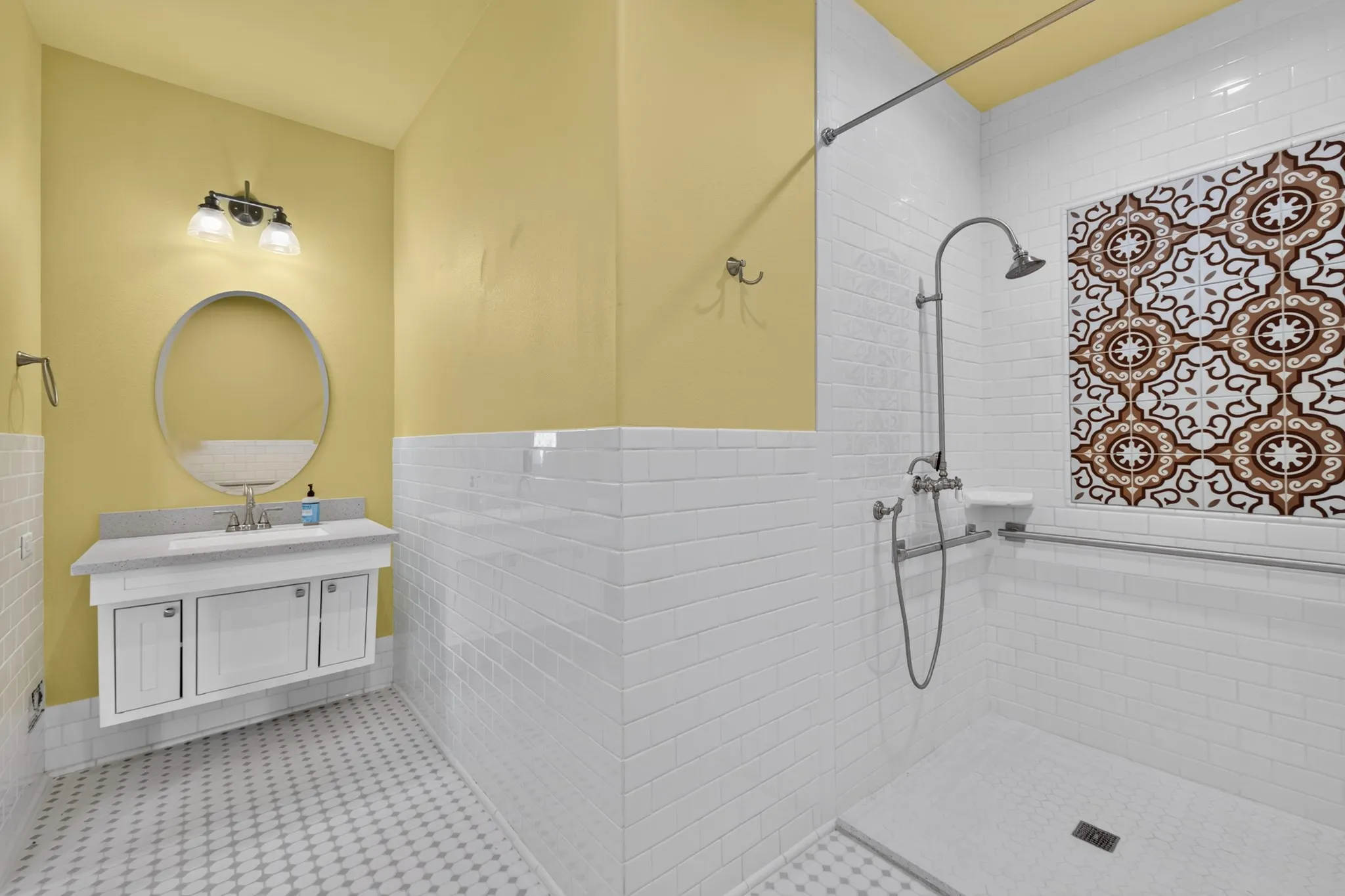 Walk-in shower with decorative tile accent, wall-mounted vanity with integrated sink, and round wall mirror