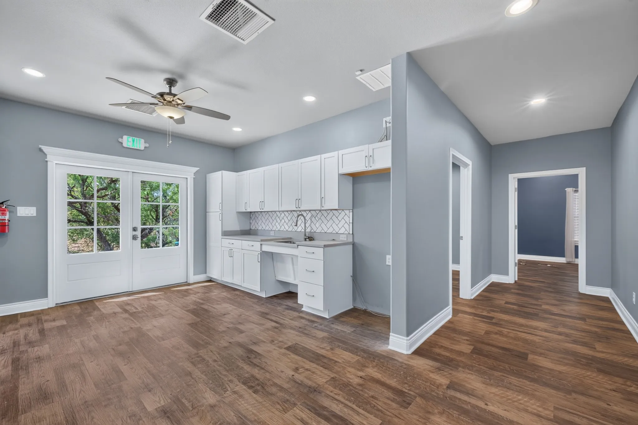 Wood-finish flooring throughout, white shaker cabinetry, herringbone tile backsplash, recessed lighting, and double-paned glass panel doors