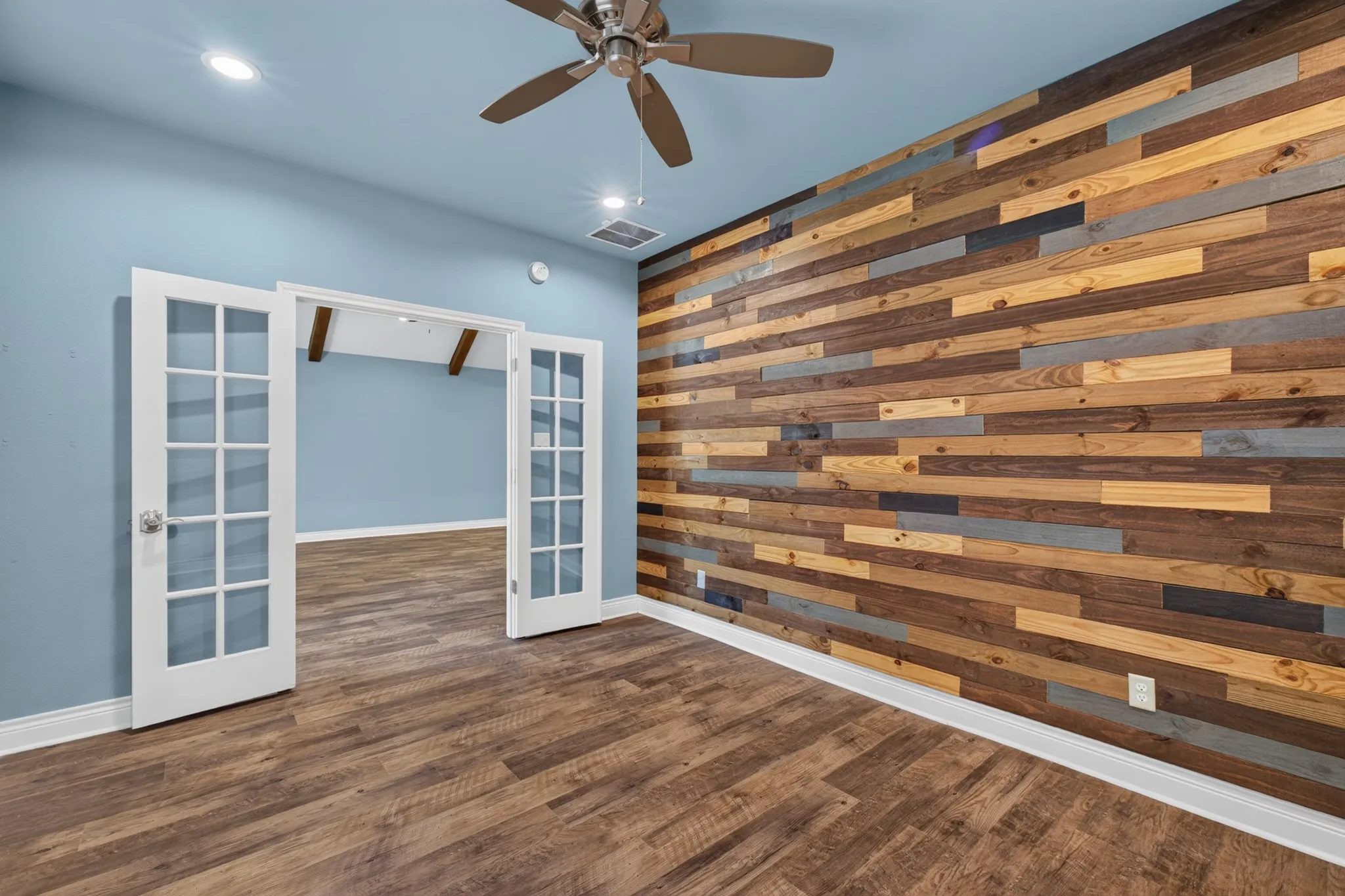 Wood-finish flooring, accent wall with varied wood paneling, recessed lighting, and a ceiling fan