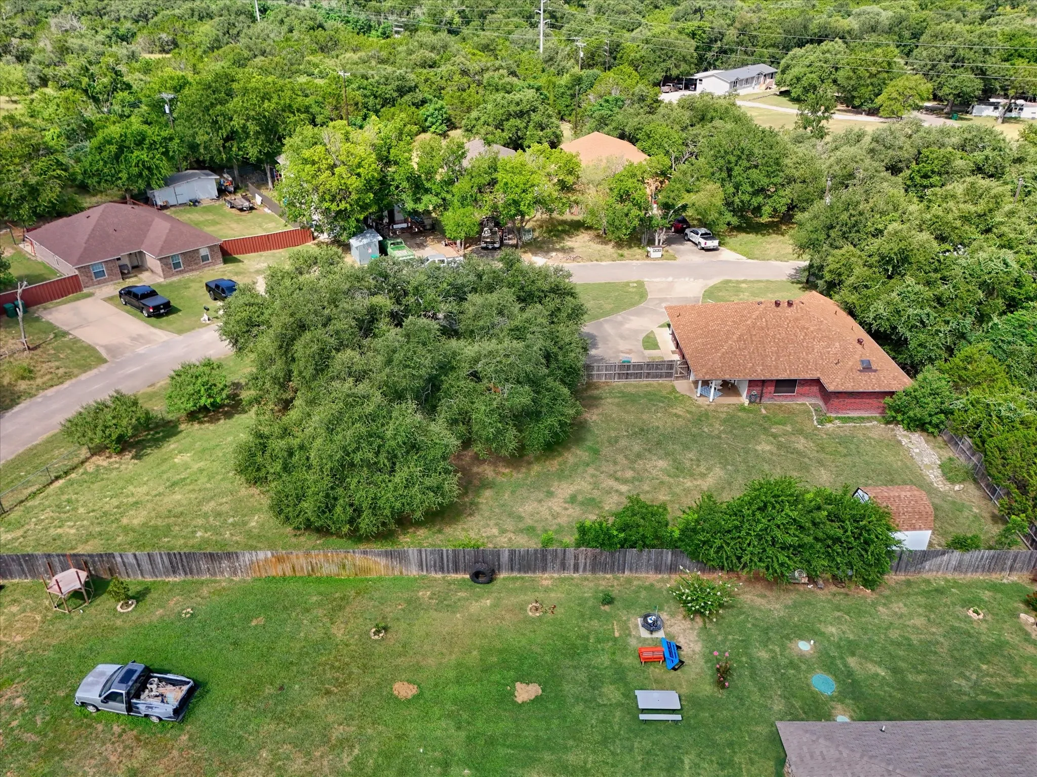 Expansive property featuring a red brick house with a brown shingled roof, a paved driveway, and mature landscaping
