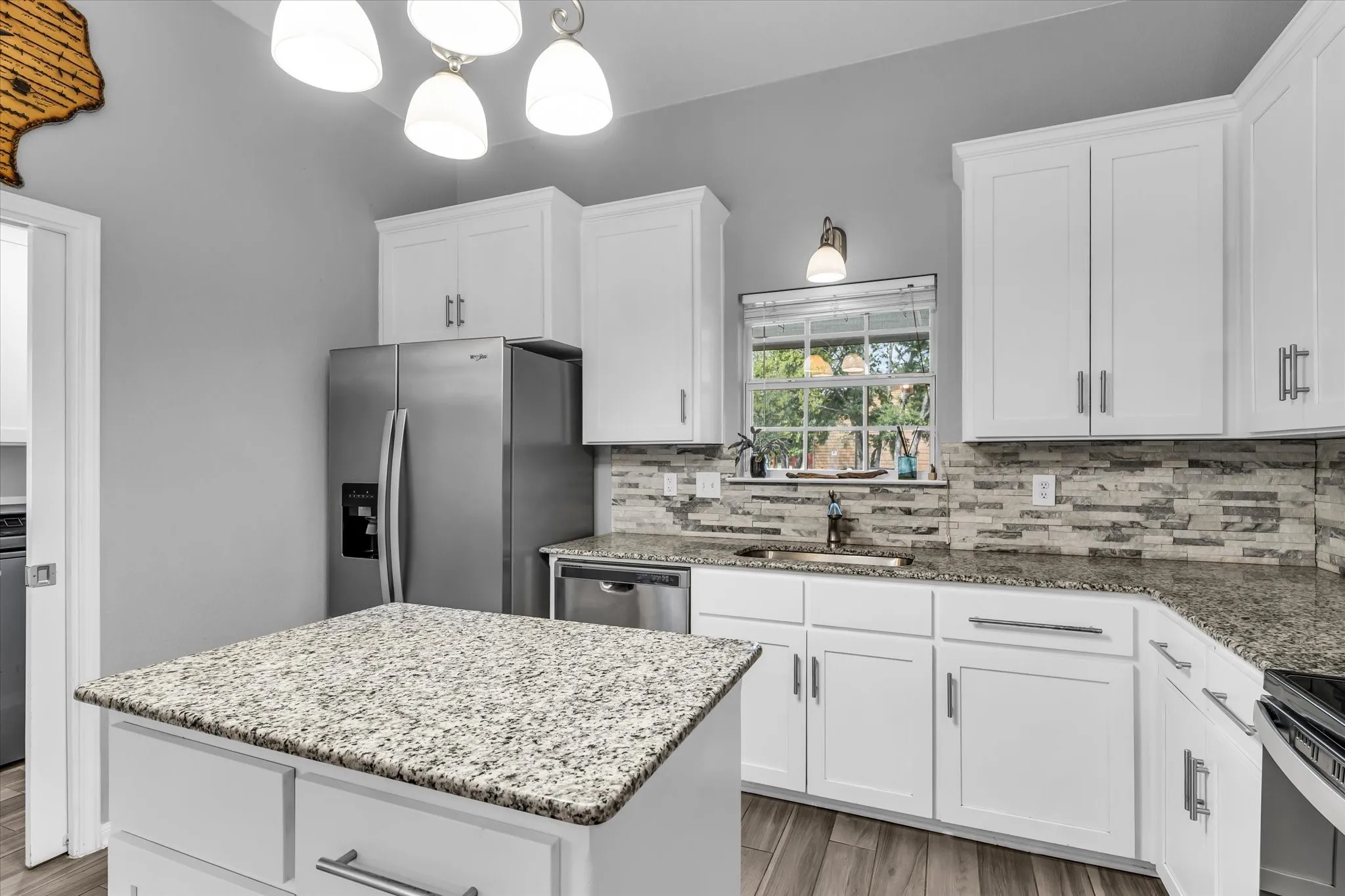Well-appointed kitchen featuring a center island with granite countertop, white cabinetry, stainless steel appliances, a tile backsplash, and wood-finish flooring