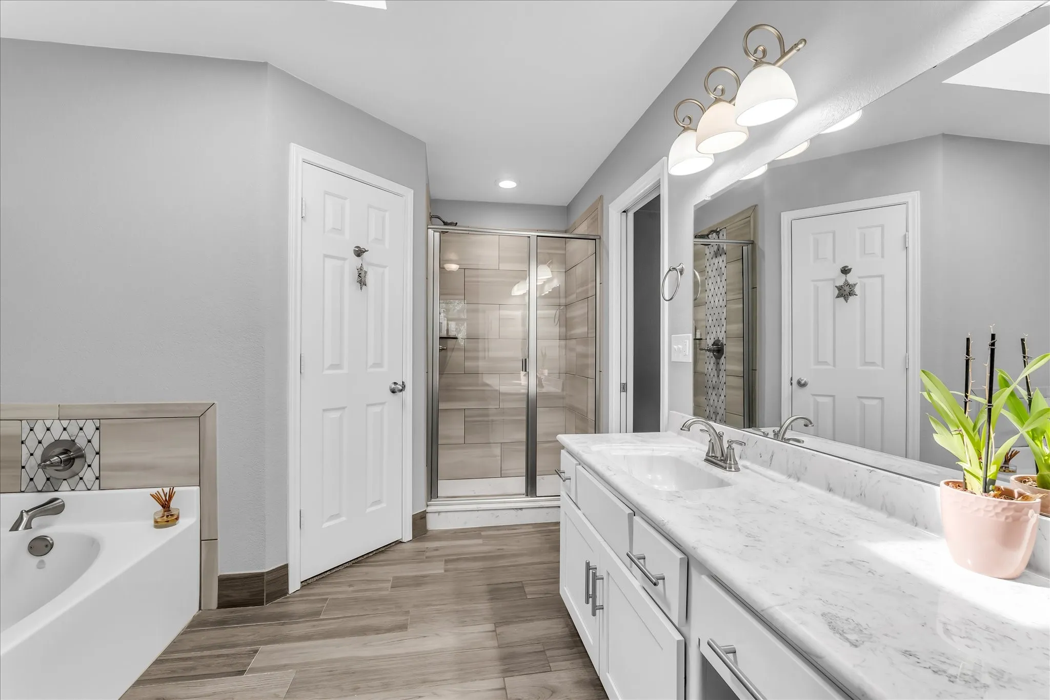 Bathroom featuring a built-in tub, faux wood-finish flooring and a white vanity with an integrated sink.